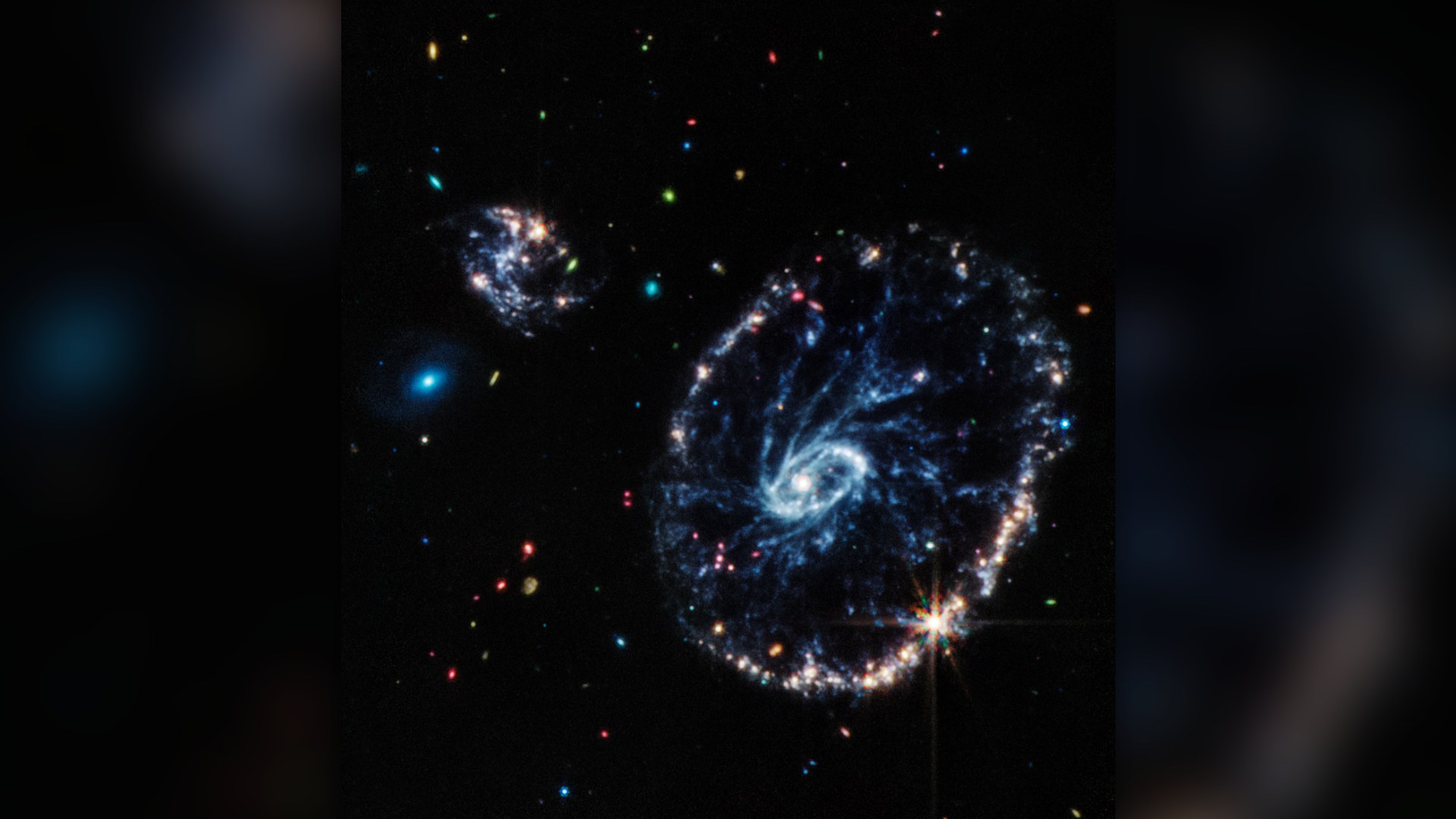 James Webb Space Telescope mid-infrared view of the Cartwheel Galaxy, showing a glowing inner ring and vast outer ring connected by dusty spokes.
