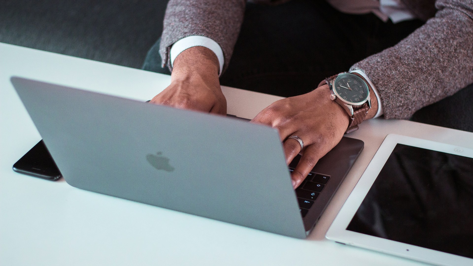 Office worker using a MacBook between an iPad and an iPhone on a corporate desk.