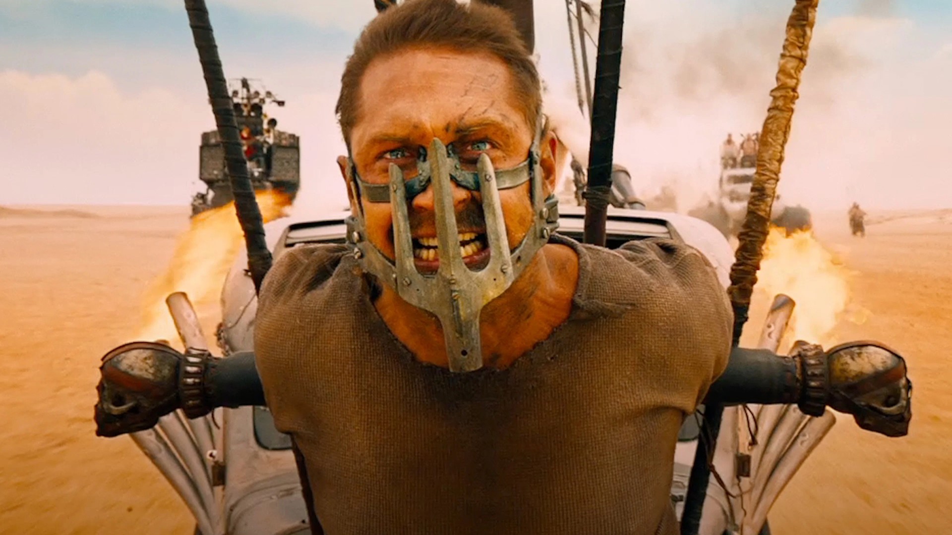 The War Rig speeds through a massive orange desert sandstorm pursued by armada vehicles in Mad Max: Fury Road.