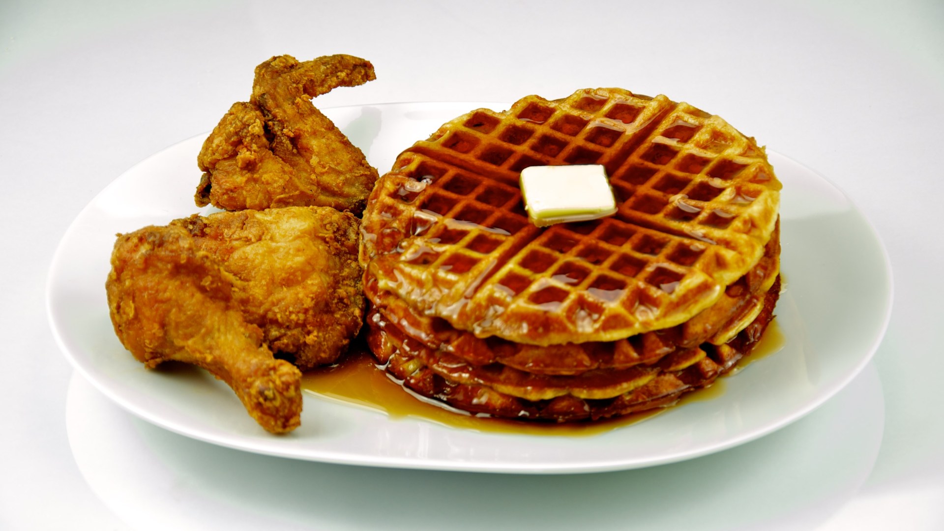 Crispy fried chicken atop golden waffles with butter and maple syrup.