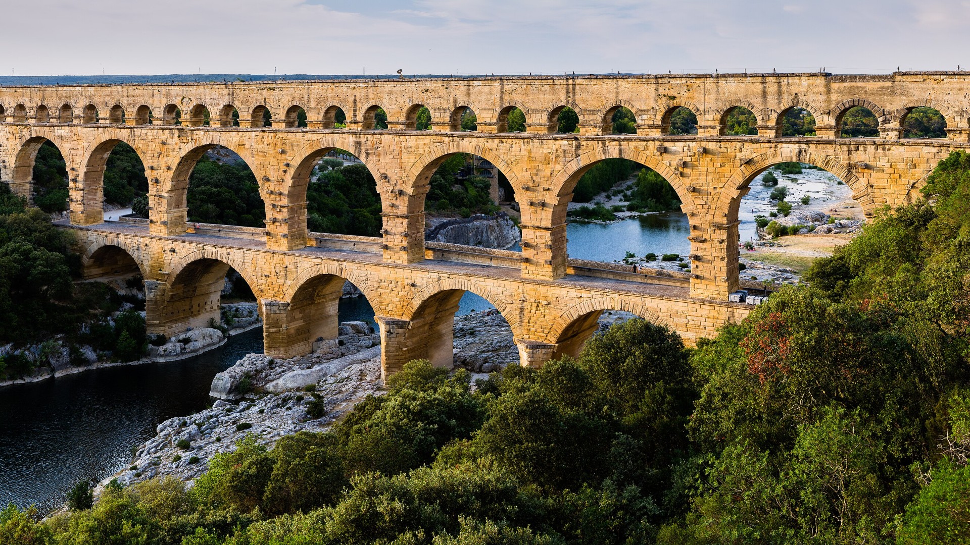 Three-tiered limestone arches of the Roman aqueduct Pont du Gard spanning the Gardon River in France.