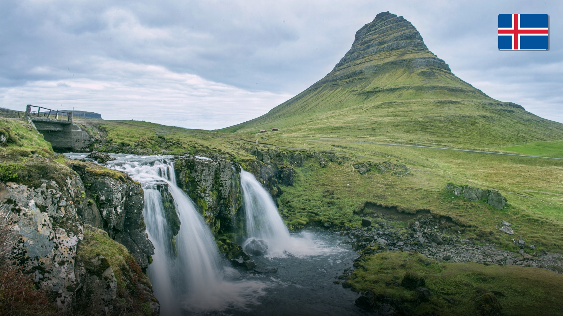 The iconic conical peak of Kirkjufell mountain framed by flowing glacial waterfalls in Iceland.