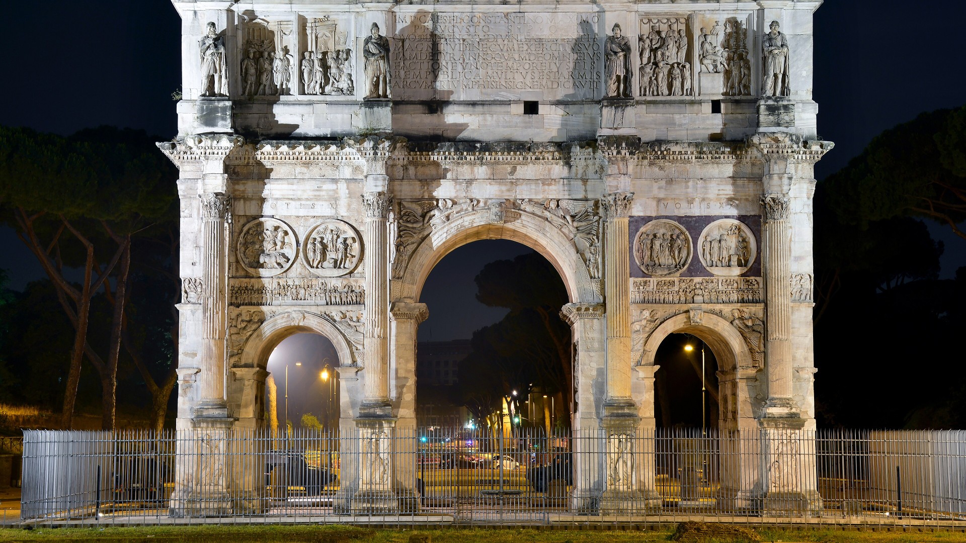 The triple-arched Roman Arch of Constantine illuminated at night in Rome.