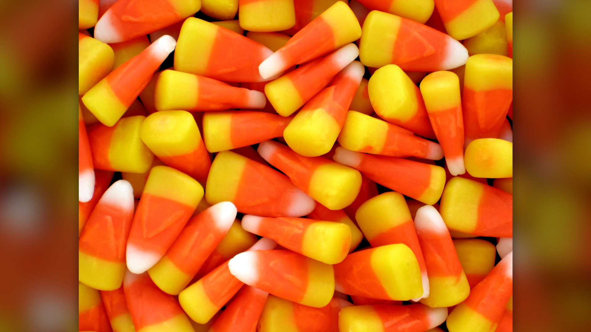 Close-up pile of yellow, orange, and white Halloween candy corn kernels.