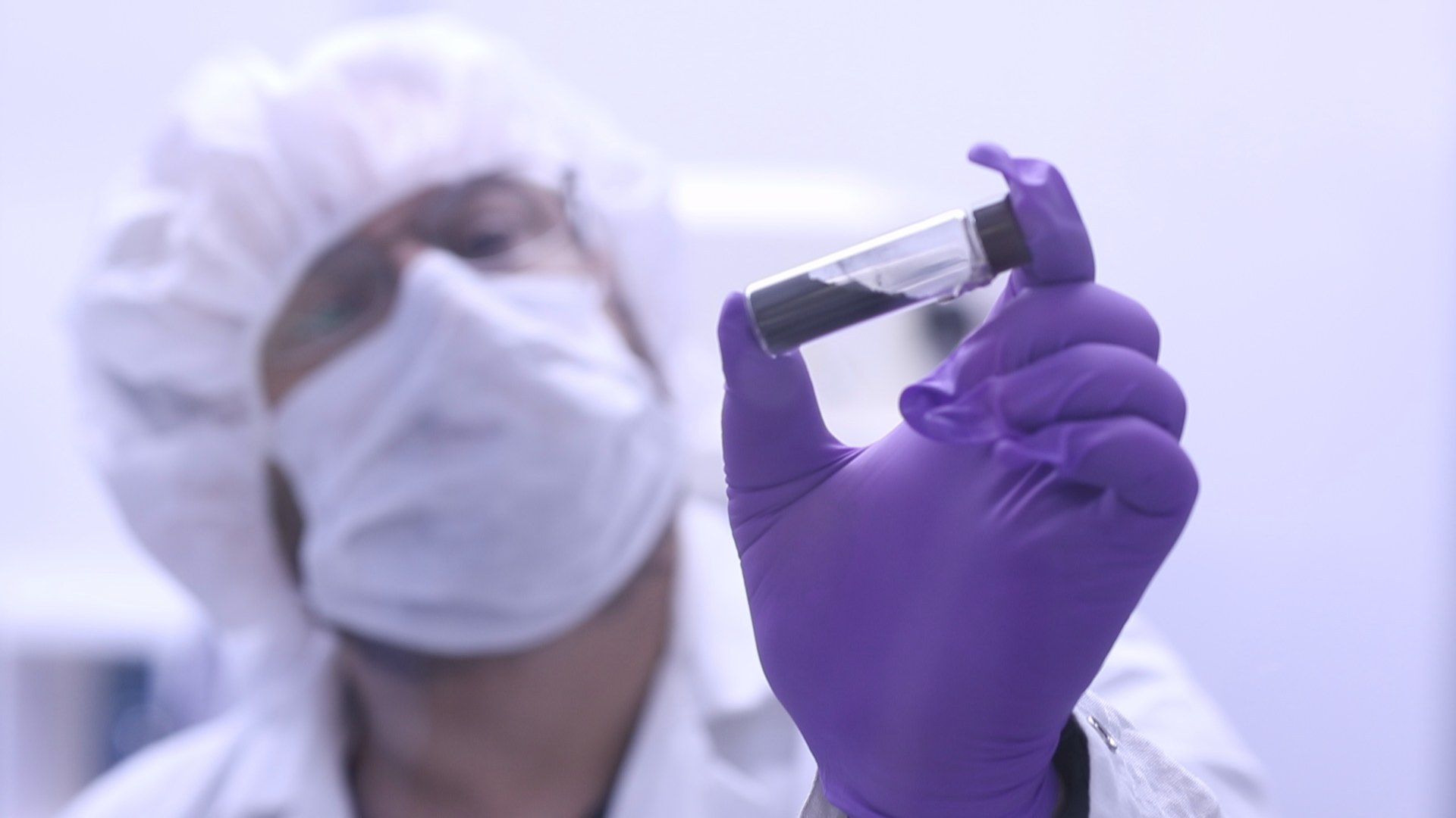 NASA scientist in a cleanroom holding a sealed glass vial of carbon-rich regolith returned from Asteroid Bennu.