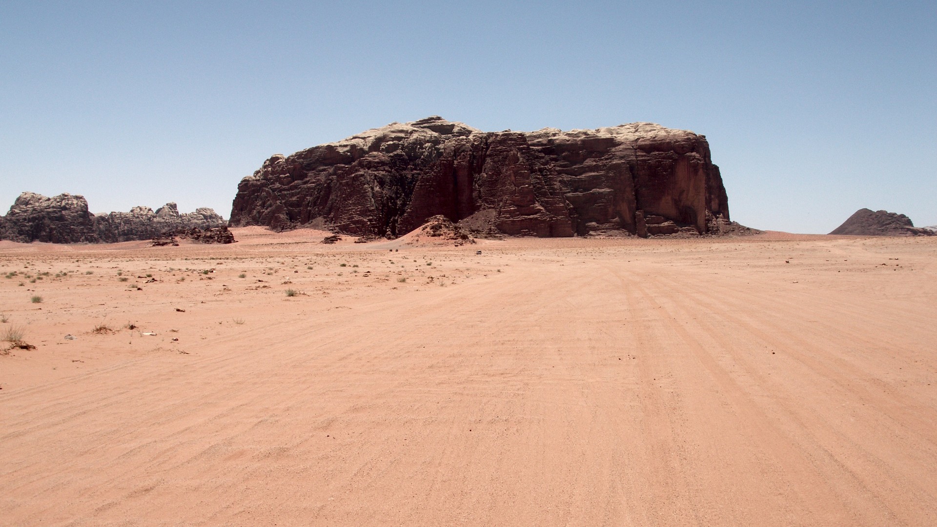 Red iron-oxide sand plains and towering sandstone cliffs in the Wadi Rum desert of Jordan.