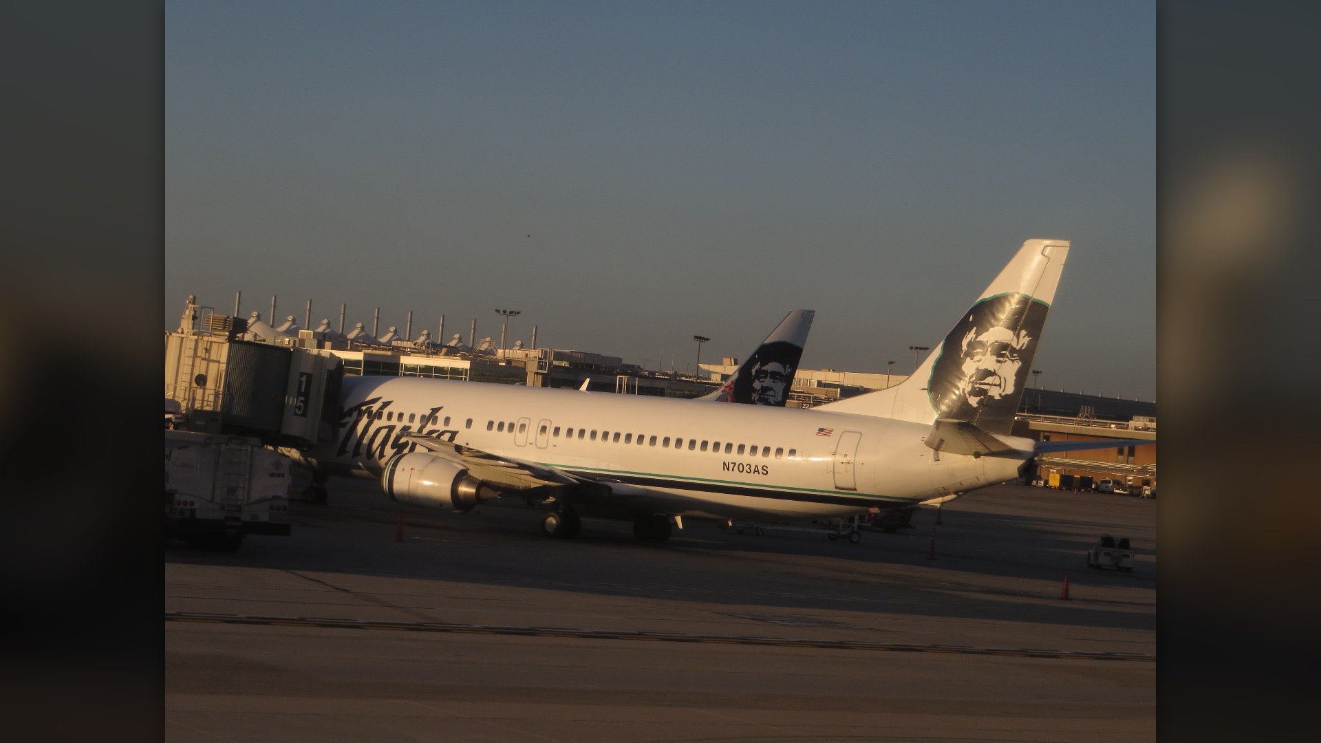 Alaska Airlines jet landing at San Diego International Airport with downtown buildings in the background.