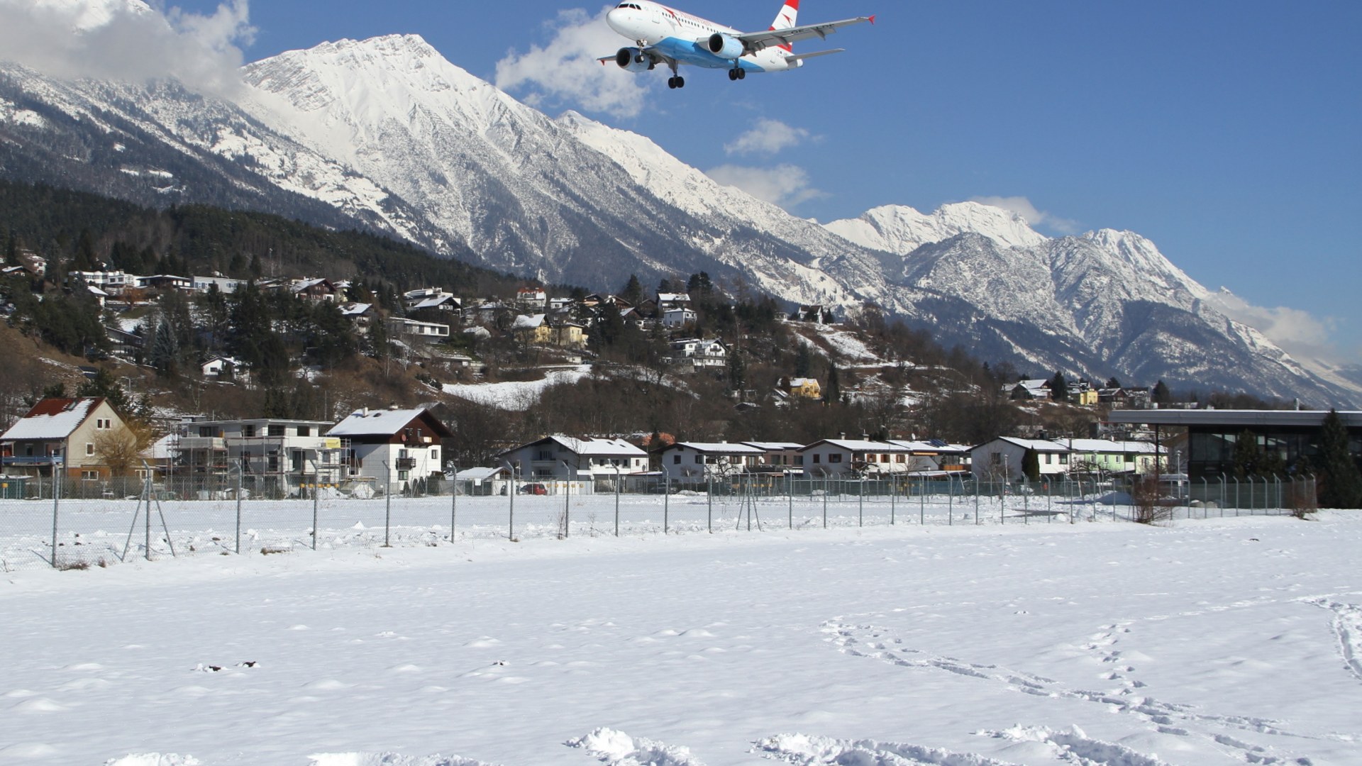 Austrian Airlines Airbus A319 landing beneath snow-capped Alpine peaks at Innsbruck Airport.