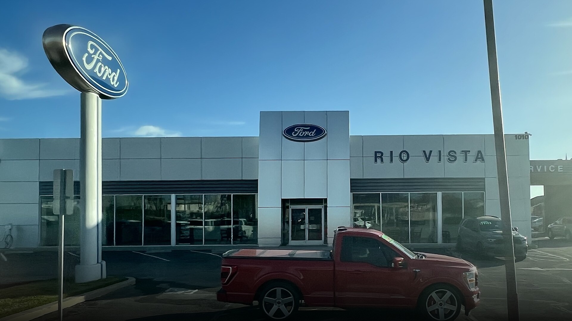 New Ford pickup truck and SUV parked outside an American Ford dealership showroom.