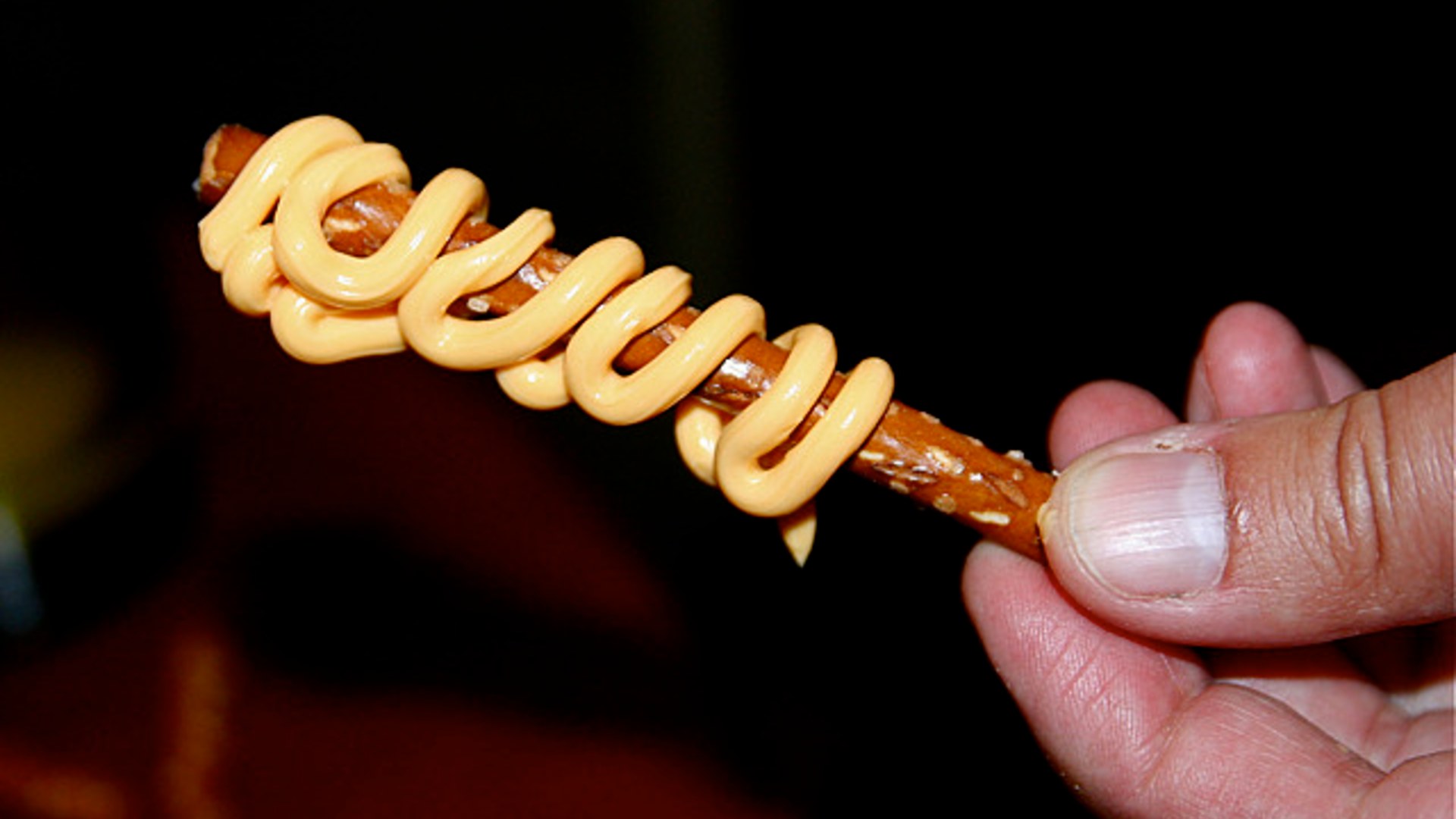 An aerosol can of Nabisco Easy Cheese spraying orange processed cheese snack onto pretzel sticks.