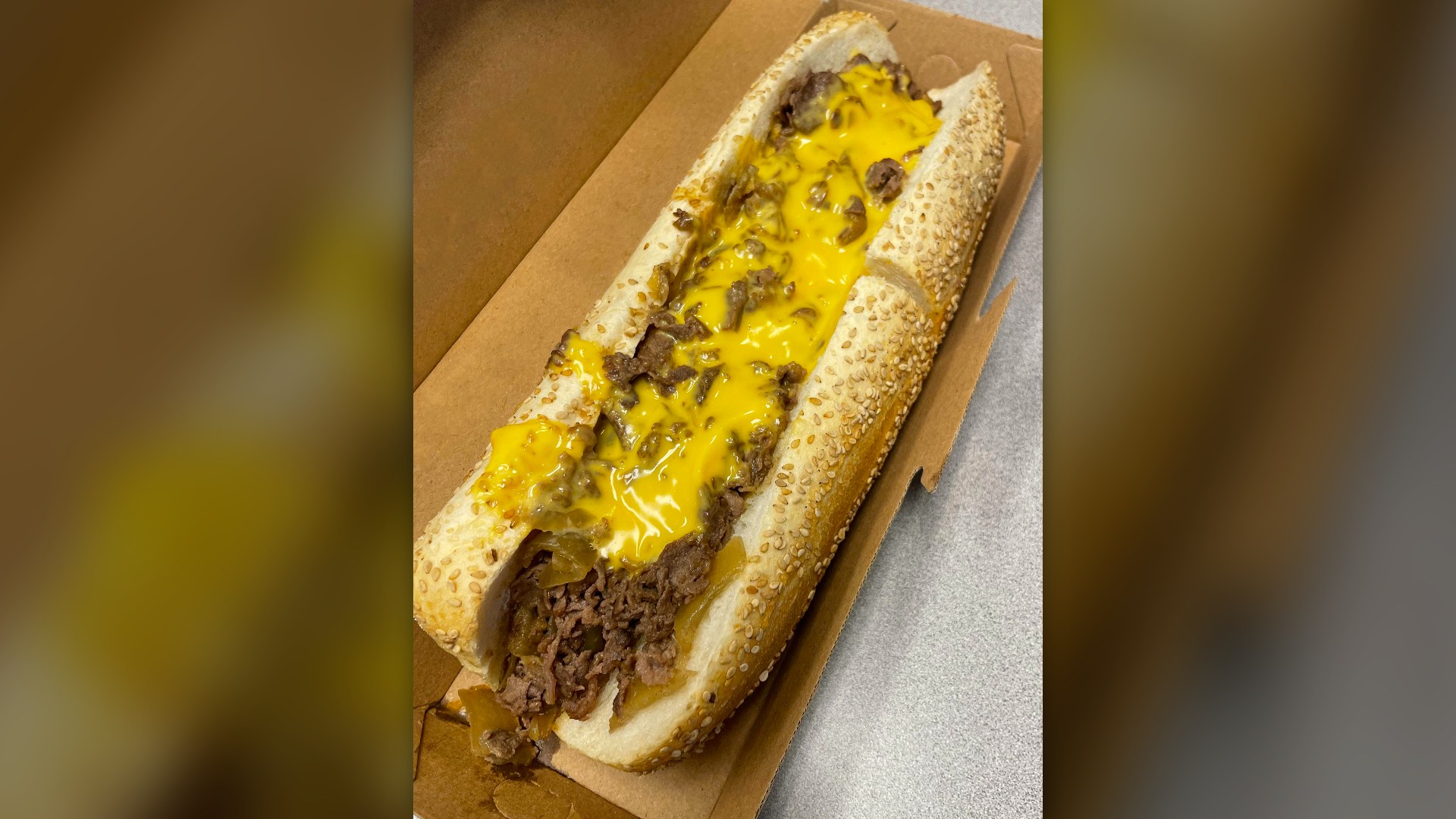 A Philadelphia cheesesteak topped with melted orange Cheez Whiz on a seeded roll.