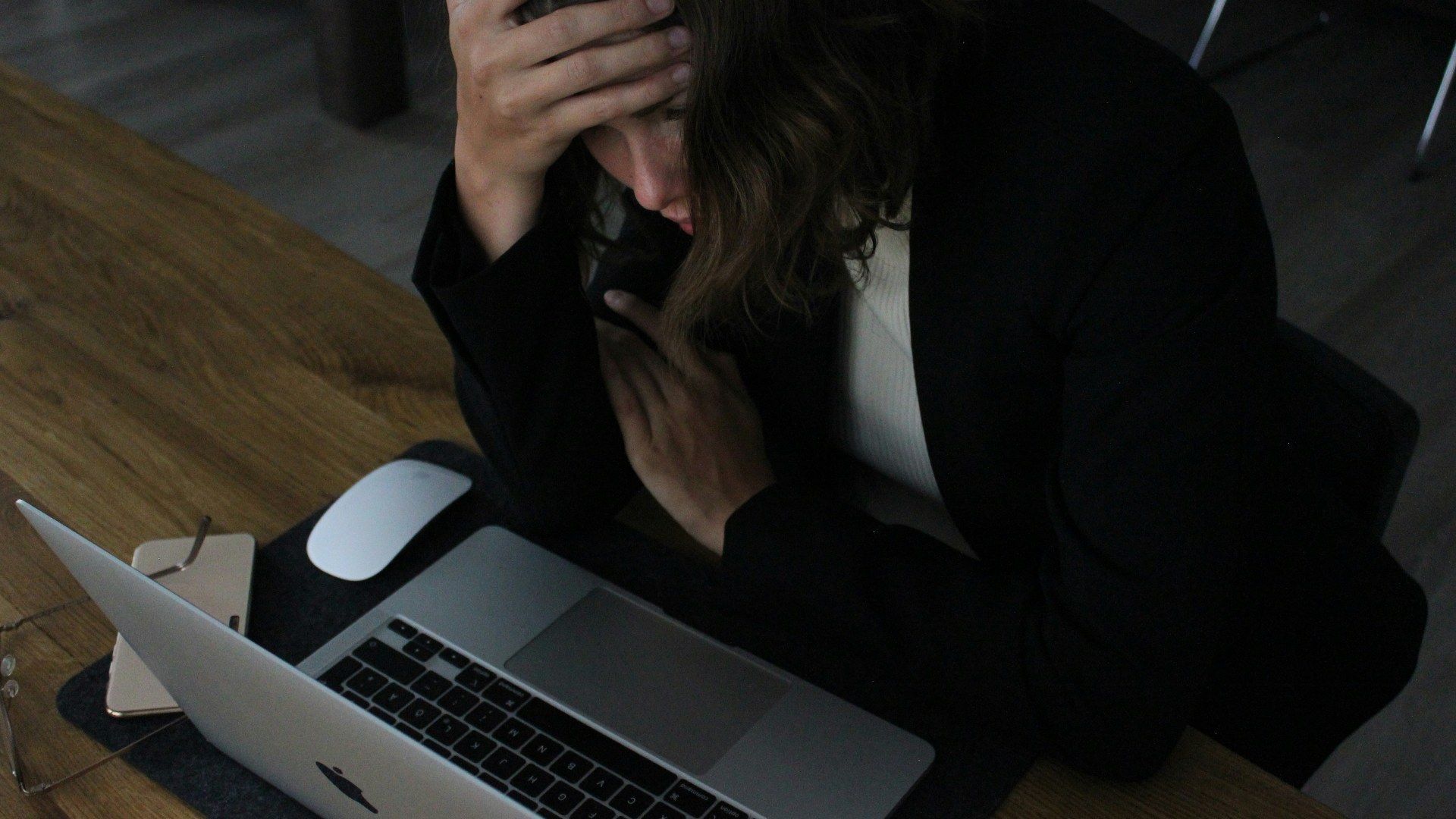 Stressed corporate woman sitting at her desk with her head in her hands in front of a laptop.