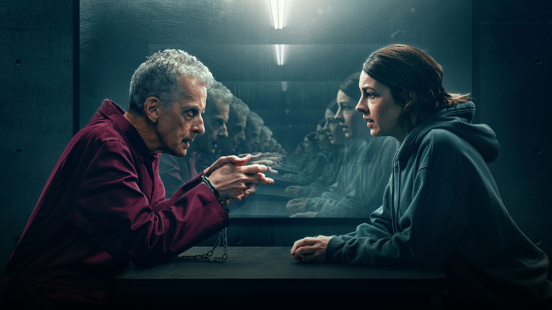 Peter Capaldi and Jessica Raine seated across a dimly lit police interrogation table.