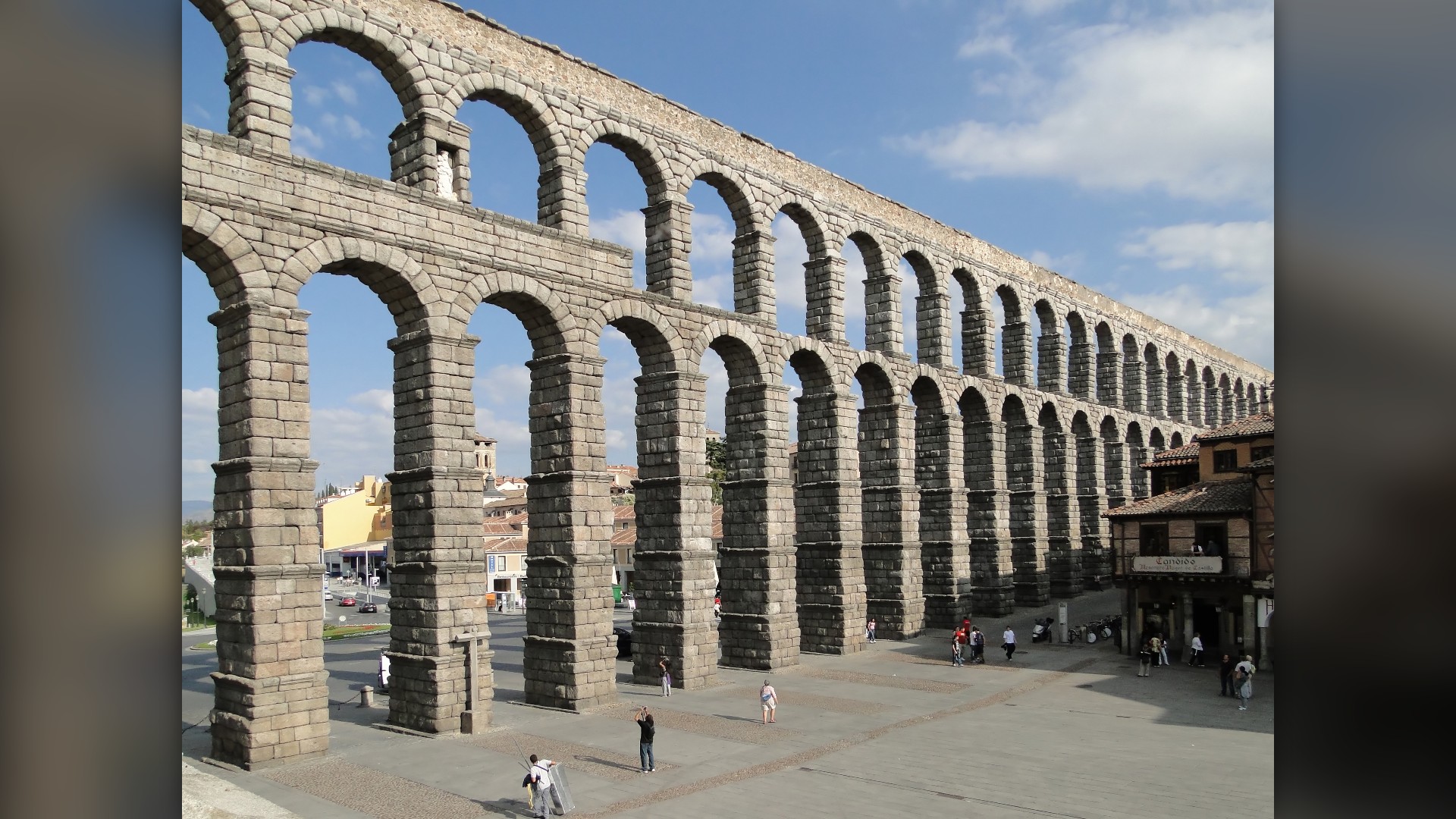 Double-tiered granite arches of the Roman Aqueduct of Segovia rising over the Spanish plaza.