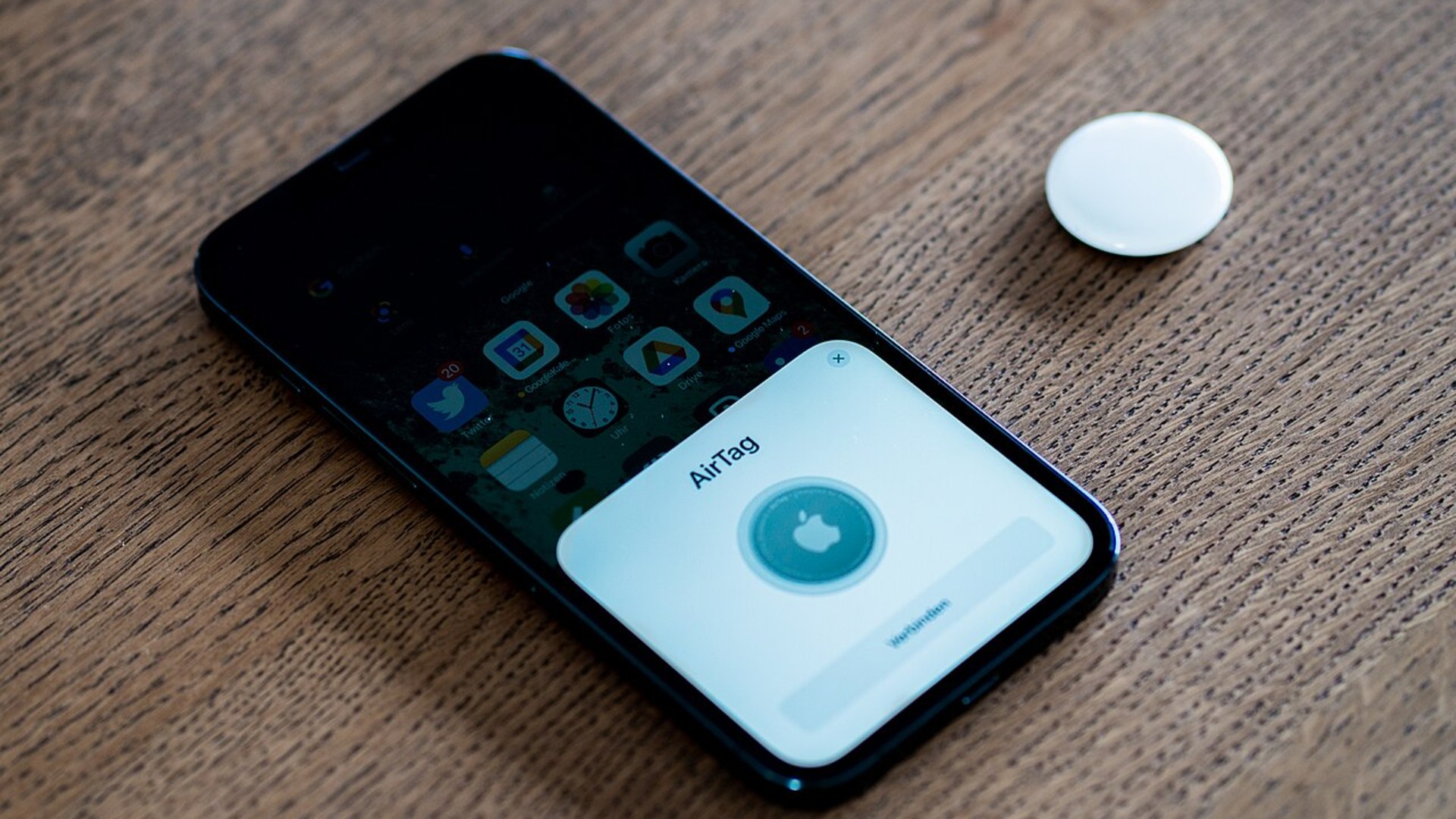 An Apple AirTag smart tracker on a table during smartphone pairing.