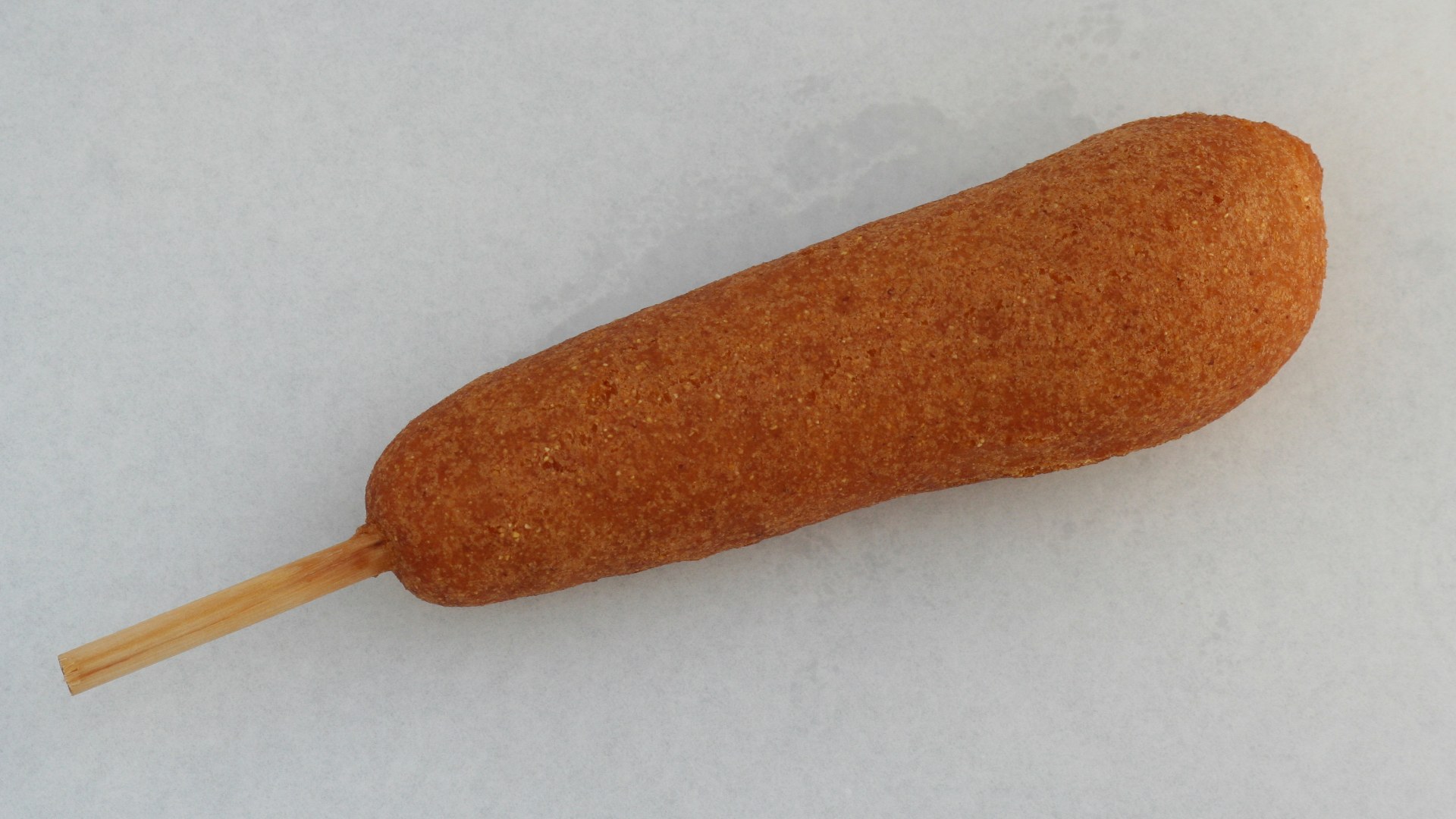 A hand-dipped corn dog on a wooden stick with mustard and ketchup.