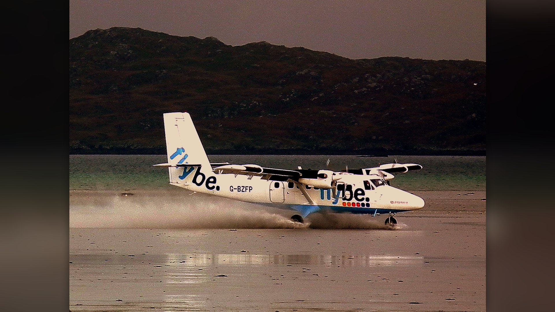 Twin Otter turboprop landing directly on the wet tidal sand beach at Barra Airport in Scotland.