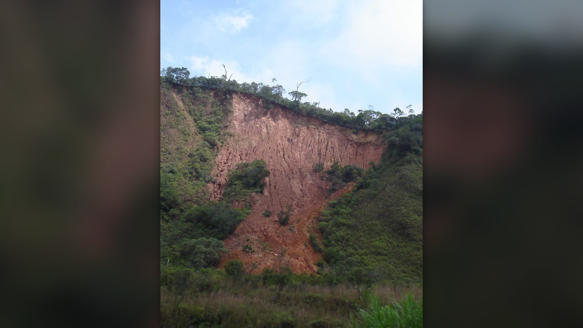 Massive red-earth hillside collapse and mudslide scar in the mountainous Petropolis-Rio de Janeiro Serrana region of Brazil.