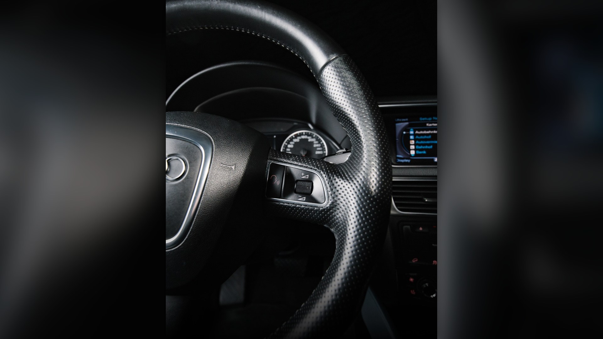 Close-up of a modern leather-wrapped car steering wheel and dashboard controls.