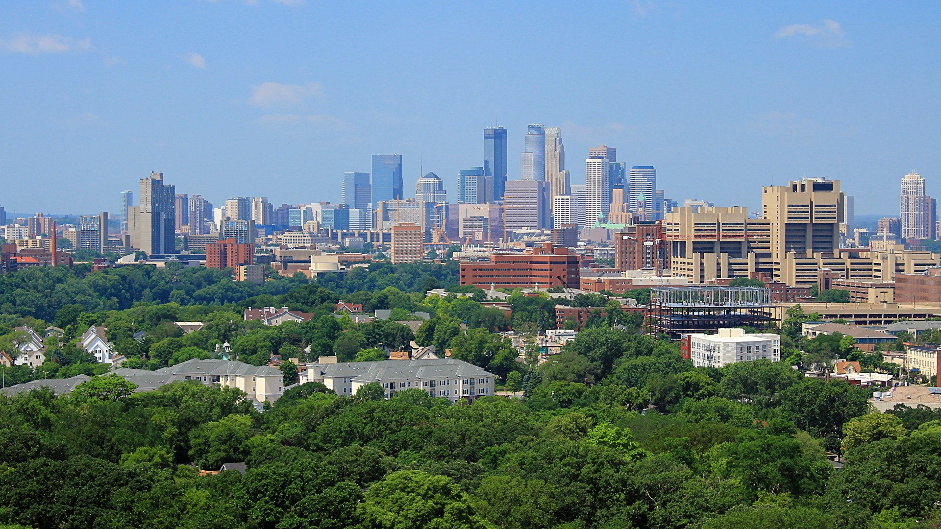 Skyline of Minneapolis, Minnesota surrounded by dense green tree canopy.