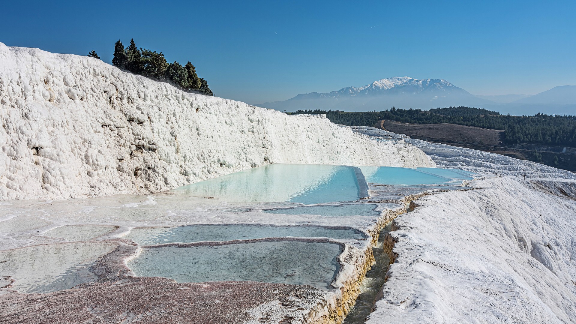 Snow-white calcium carbonate travertine terraces filled with turquoise thermal water in Pamukkale, Turkey.