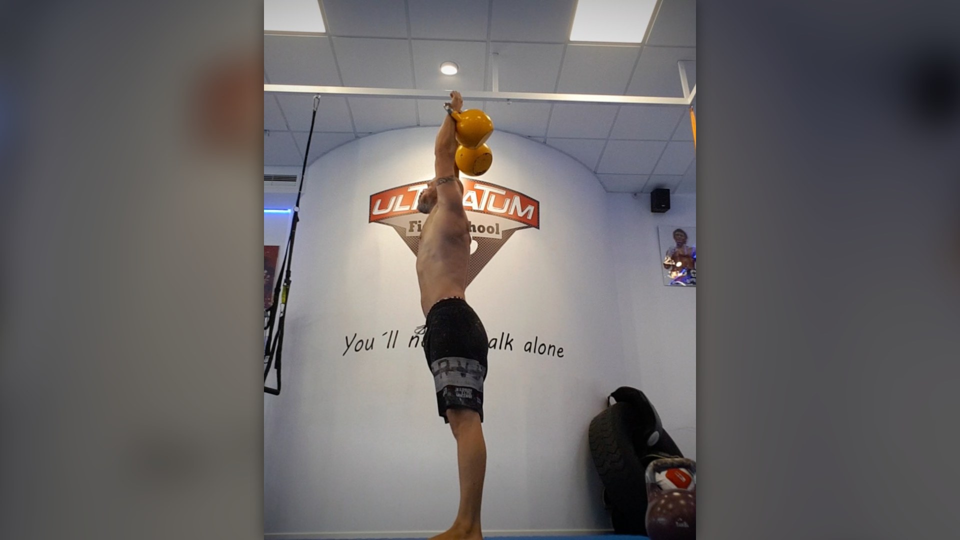 Athlete demonstrating kettlebell clean and jerk lockout in gym.
