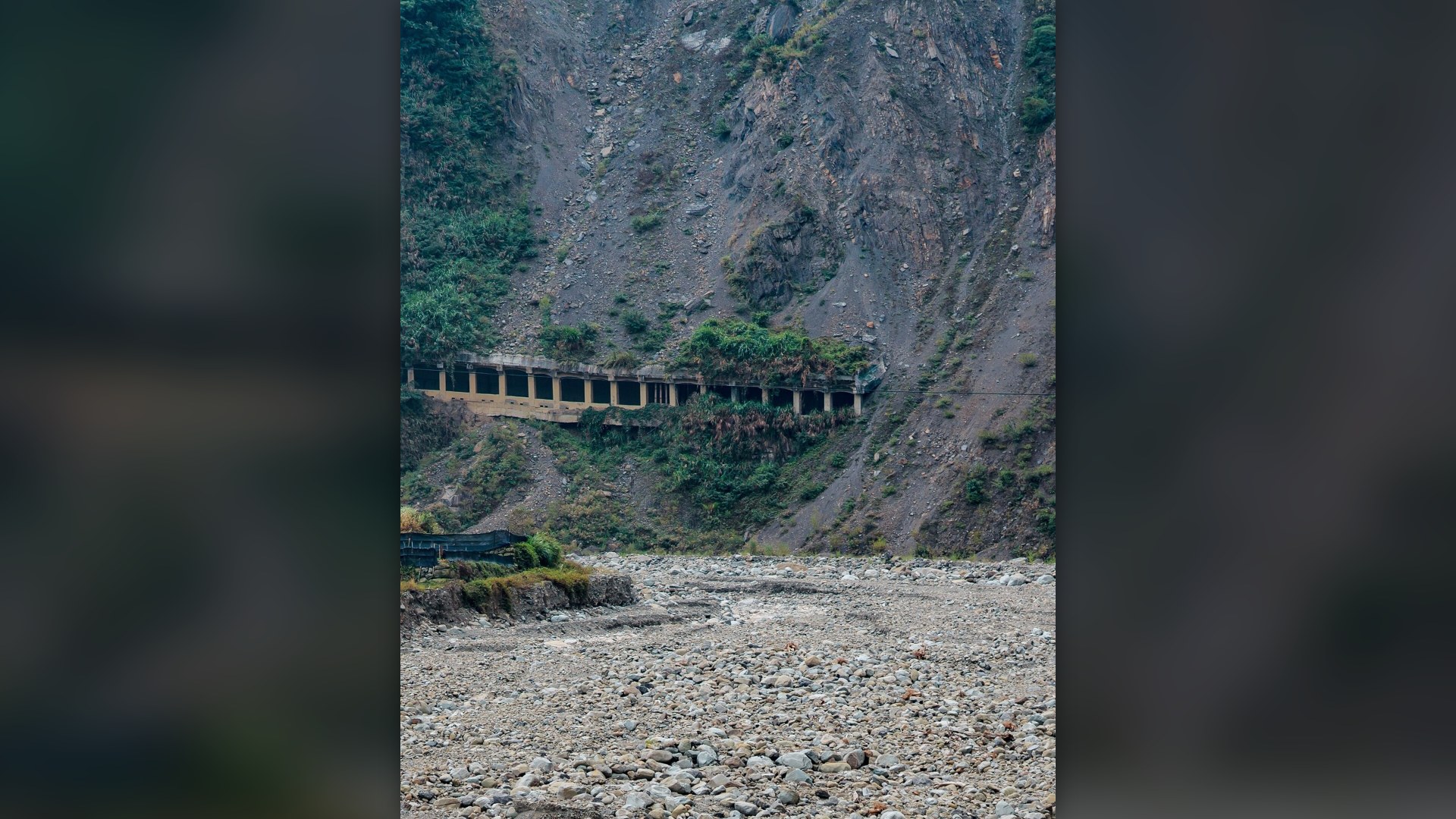 Collapsed mountainside and rockslide burying a highway gallery along a river valley in Taiwan.