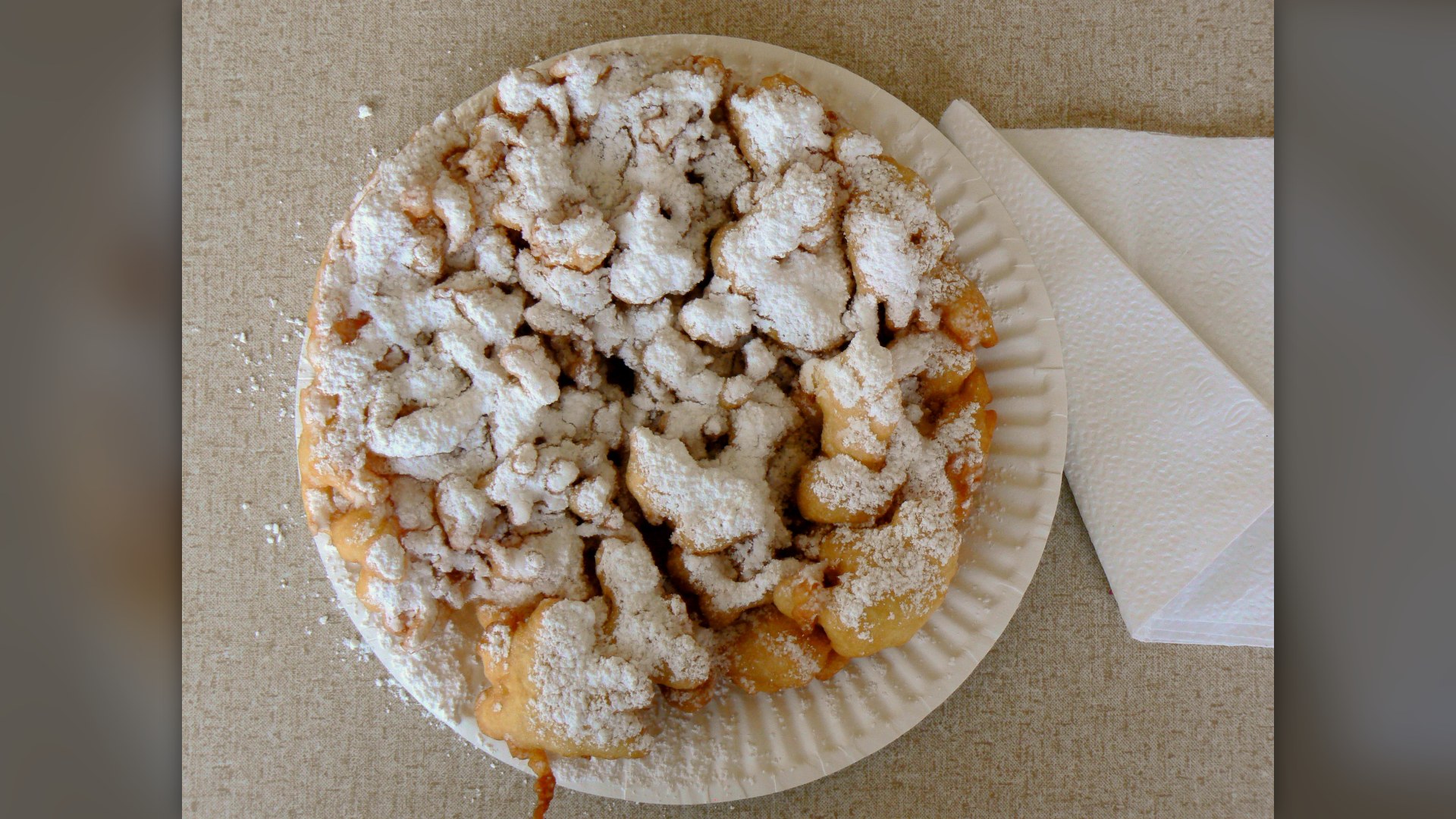 A state fair funnel cake covered in powdered sugar on a paper plate.