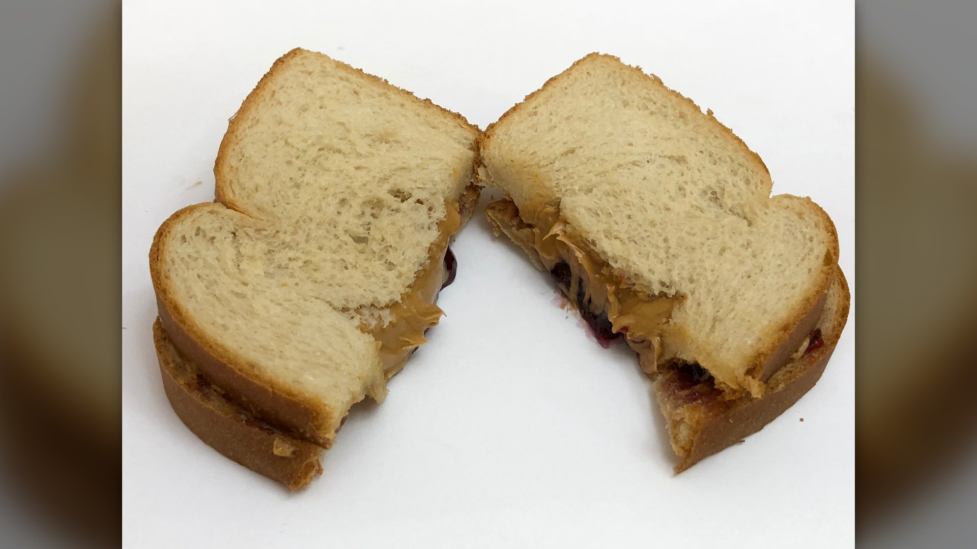 A peanut butter and Concord grape jelly sandwich cut in half.