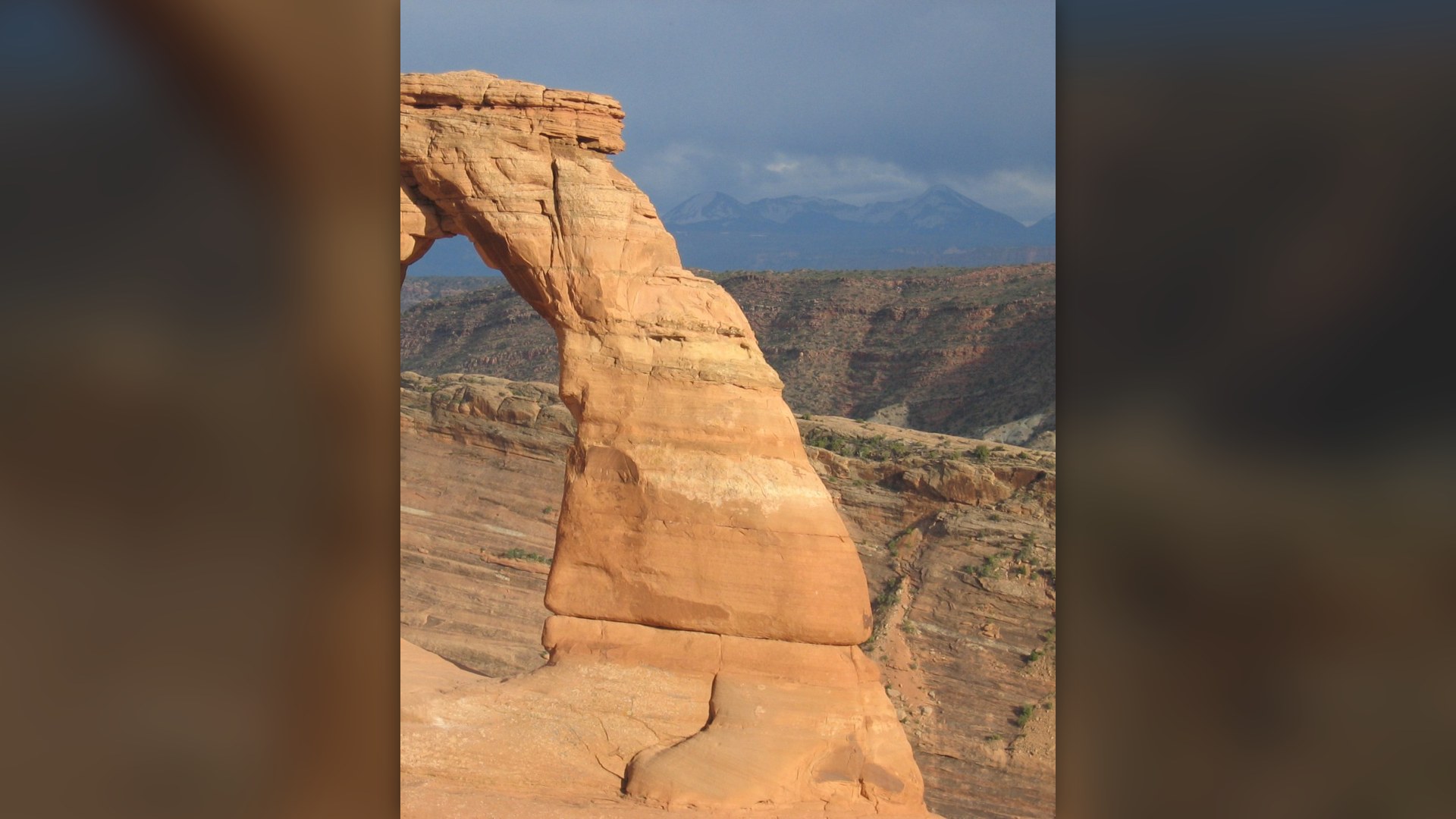 Natural red sandstone arch of Delicate Arch framed against snow-capped mountains in Arches National Park, Utah.