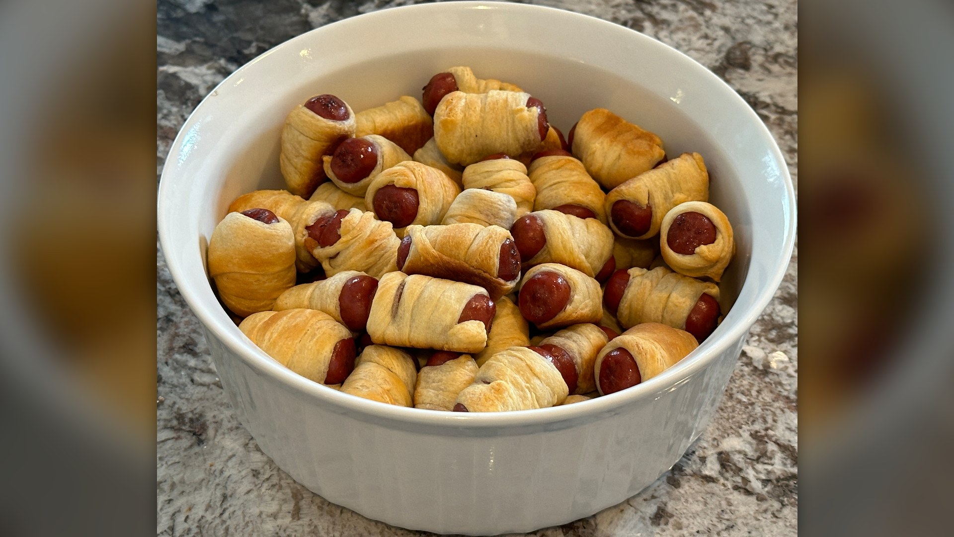 A bowl of American-style pigs in a blanket wrapped in crescent roll dough.