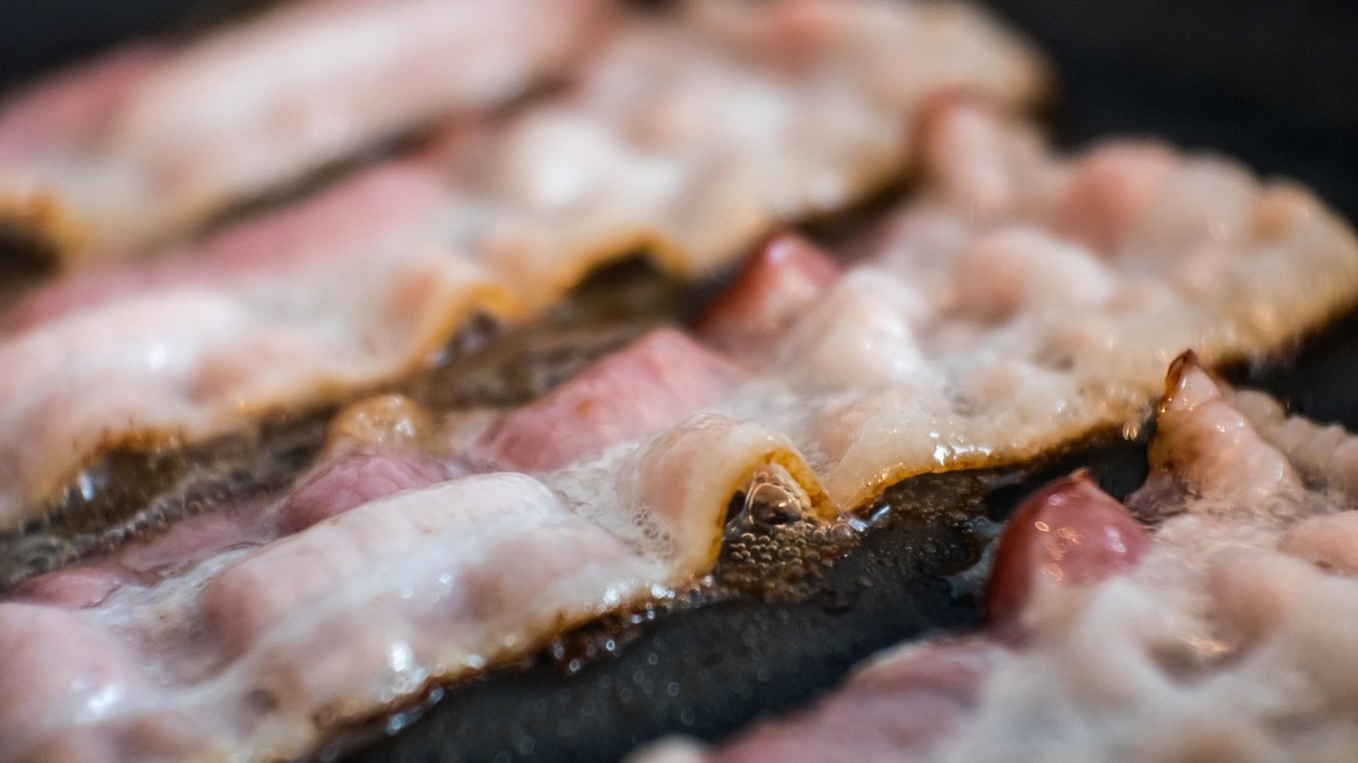 Crispy fried bacon strips sizzling in a pan