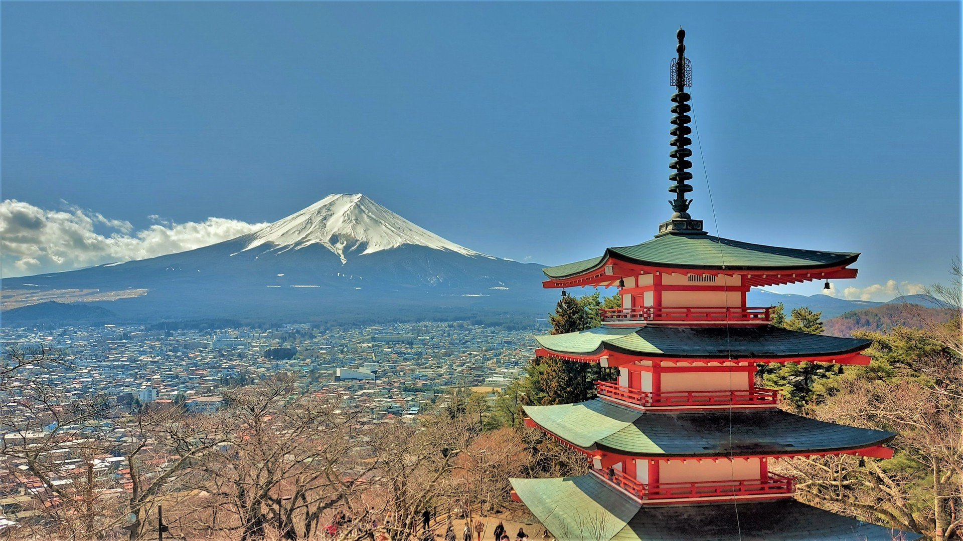 The iconic red five-story Chureito Pagoda framing the snow-capped peak of Mount Fuji under a brilliant blue sky.