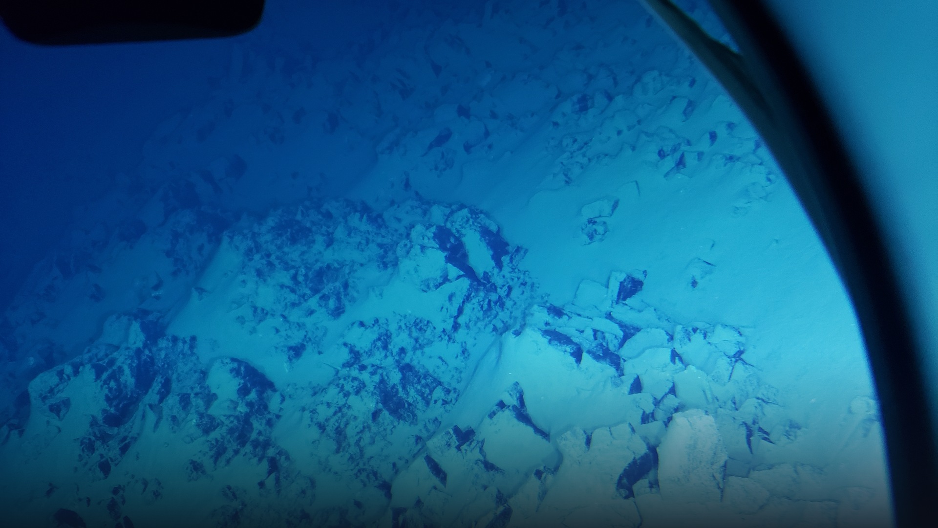 Deep-sea submersible exterior view illuminating the rocky abyssal wall of Challenger Deep at the bottom of Mariana Trench.