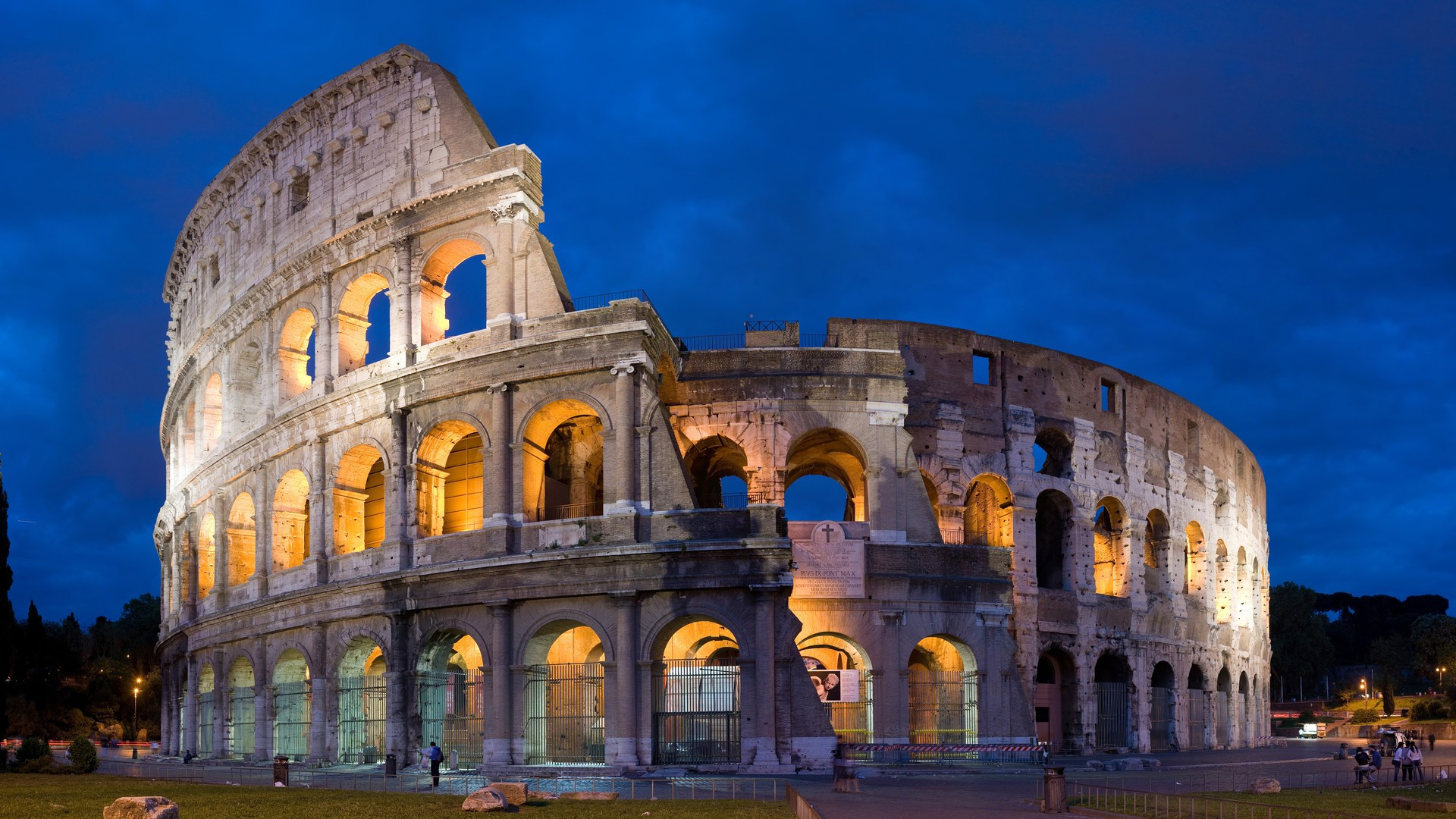 The illuminated arches and ancient stone facade of the Colosseum in Rome under an evening twilight sky.