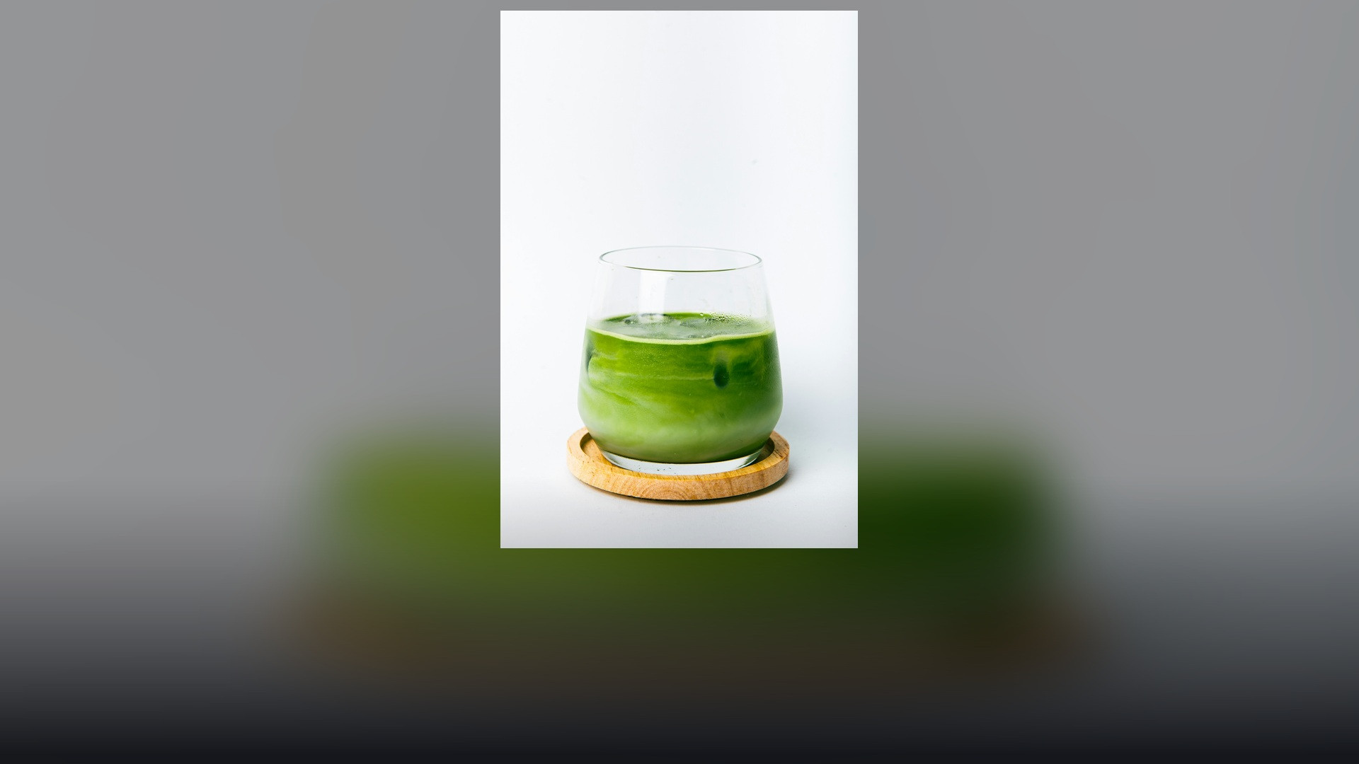 Bright, vibrant layered green iced matcha beverage in tall glassware resting on a natural wooden coaster.