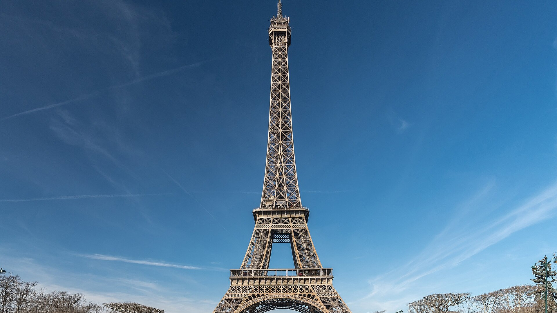 The majestic iron lattice Eiffel Tower rising straight into a pristine blue Parisian summer sky.