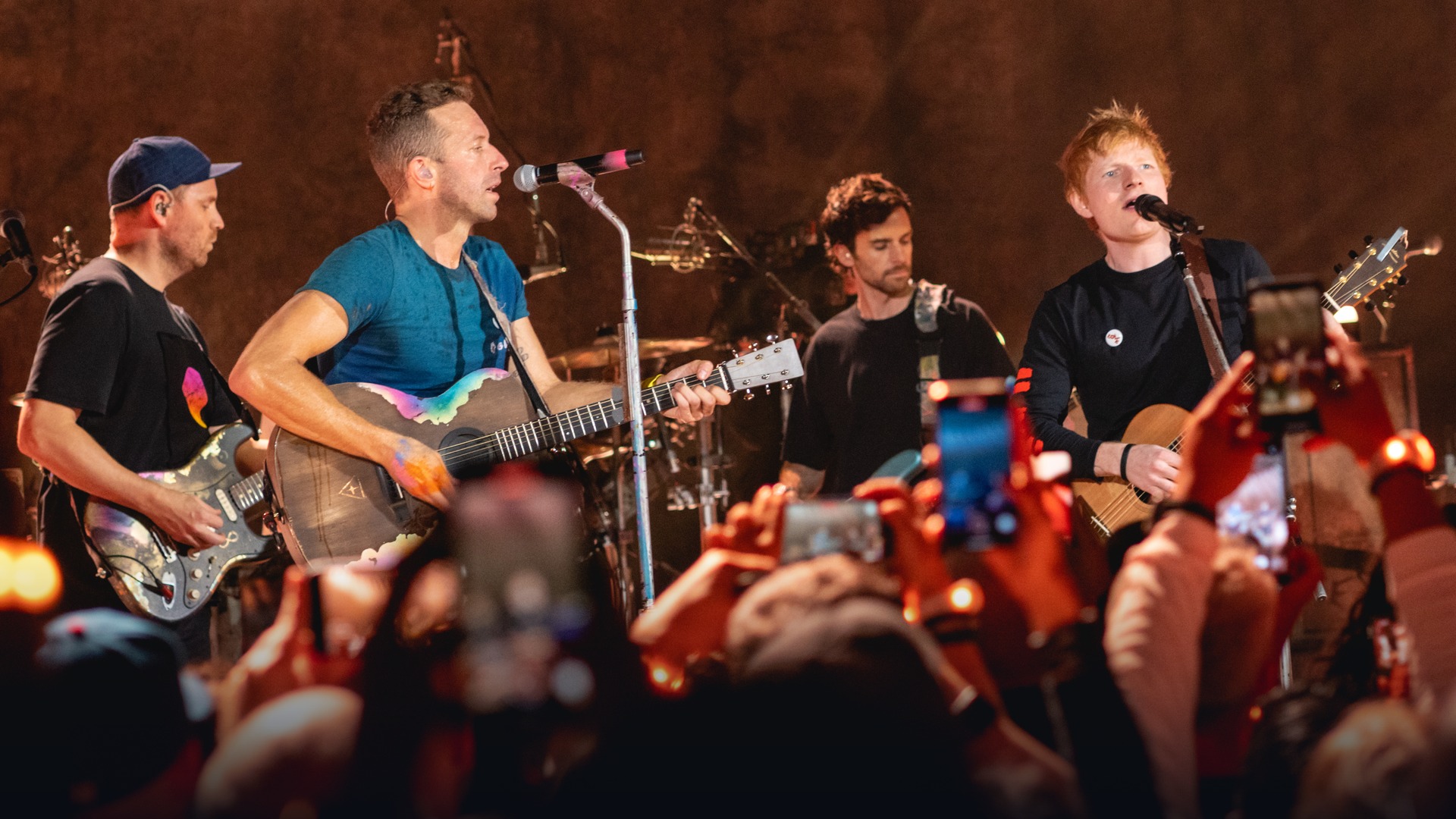 Ed Sheeran performing alongside stadium headliners under arena lights.
