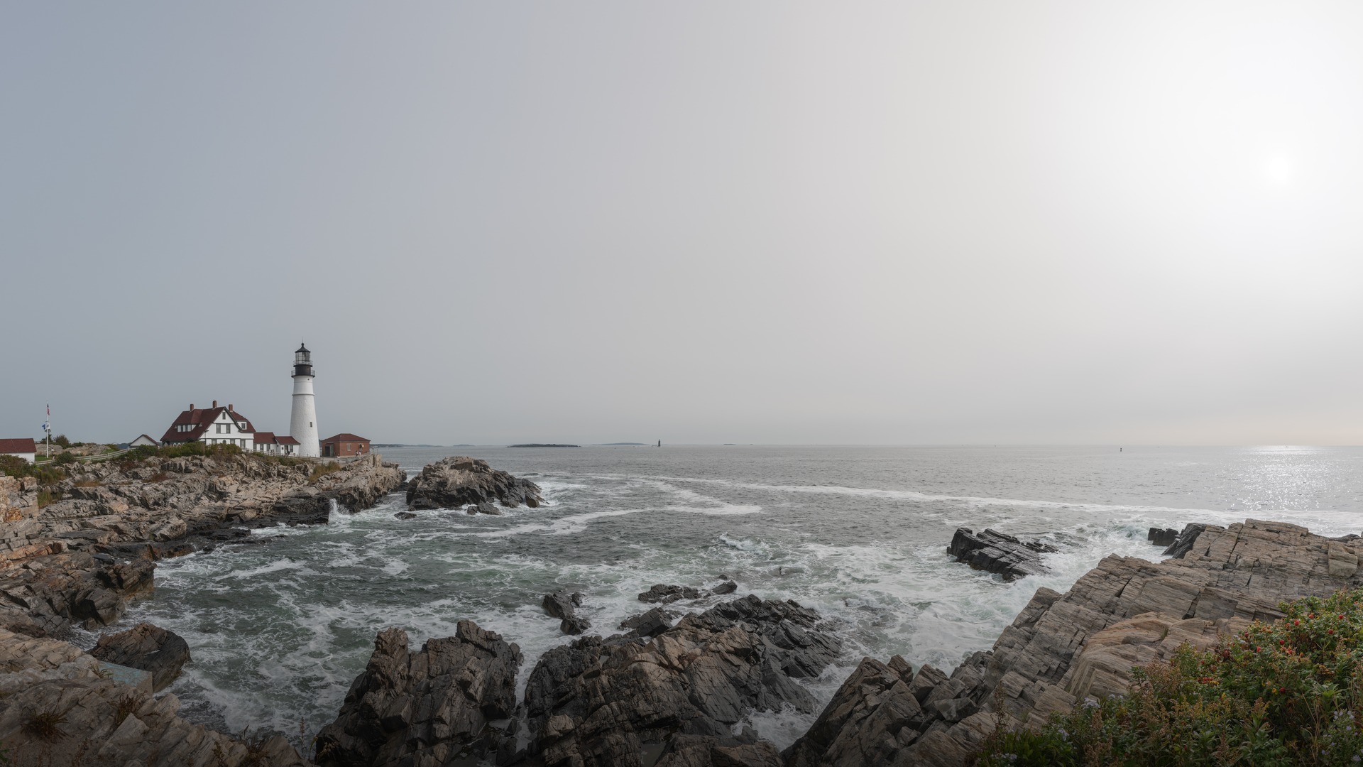 The historic white lighthouse tower of Portland Head Light standing atop rocky coastal cliffs overlooking the ocean in Cape Elizabeth Maine.