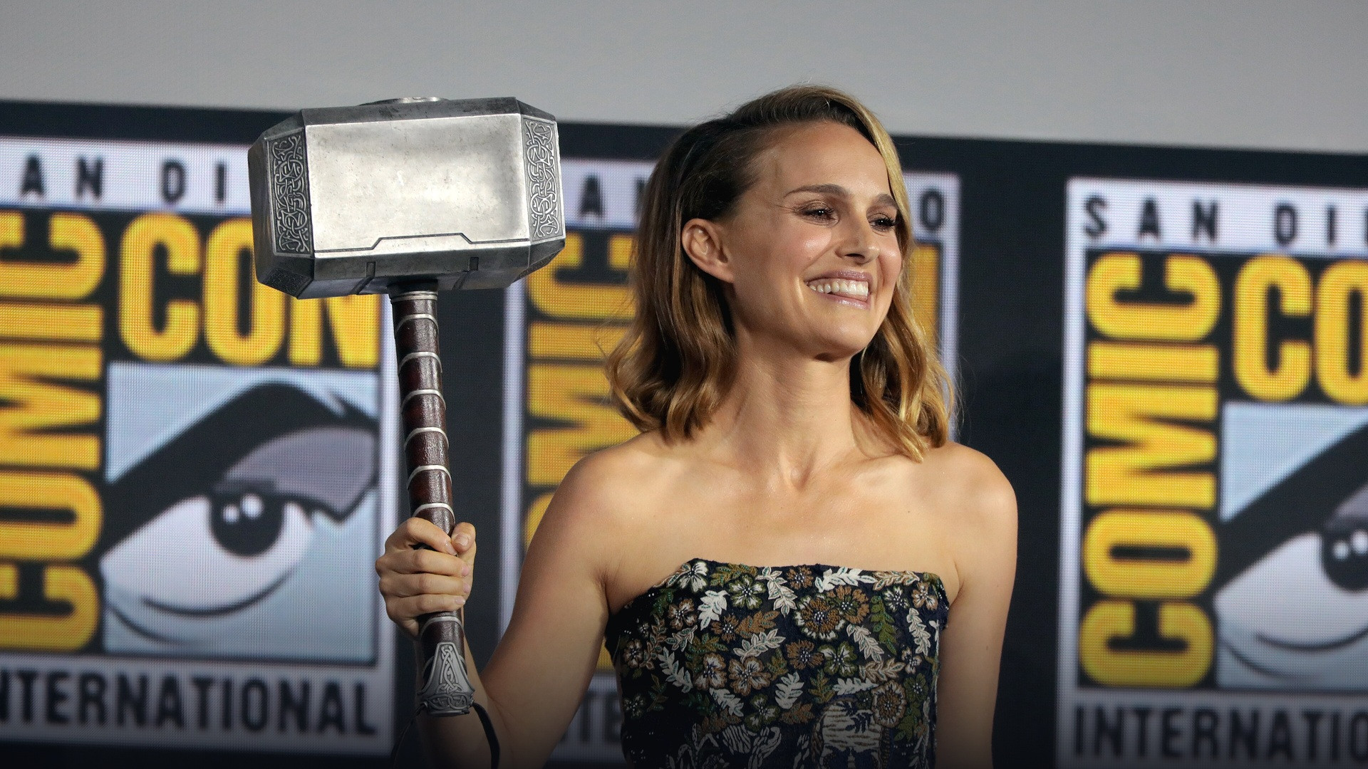 Natalie Portman holding up Thor's hammer Mjolnir on stage at San Diego Comic-Con