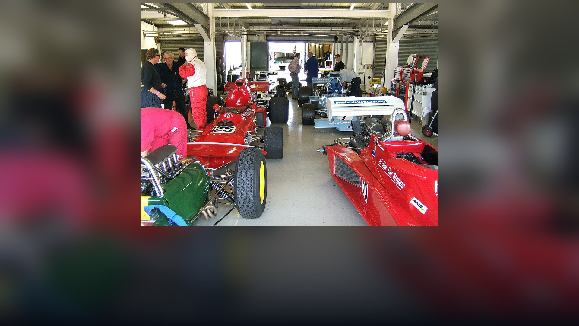 Formula One technical pit garage with engineers assembling aerodynamic chassis components.