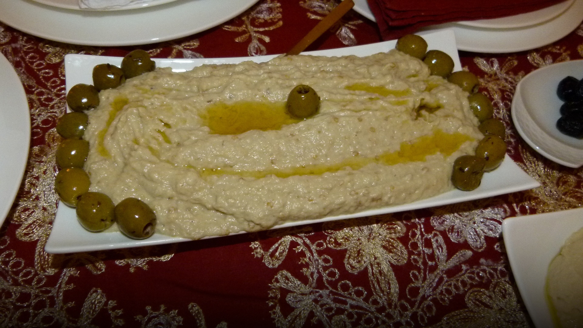 A decorated bowl of creamy smoky roasted eggplant dip drizzled with extra virgin olive oil, olives, and fresh herbs.