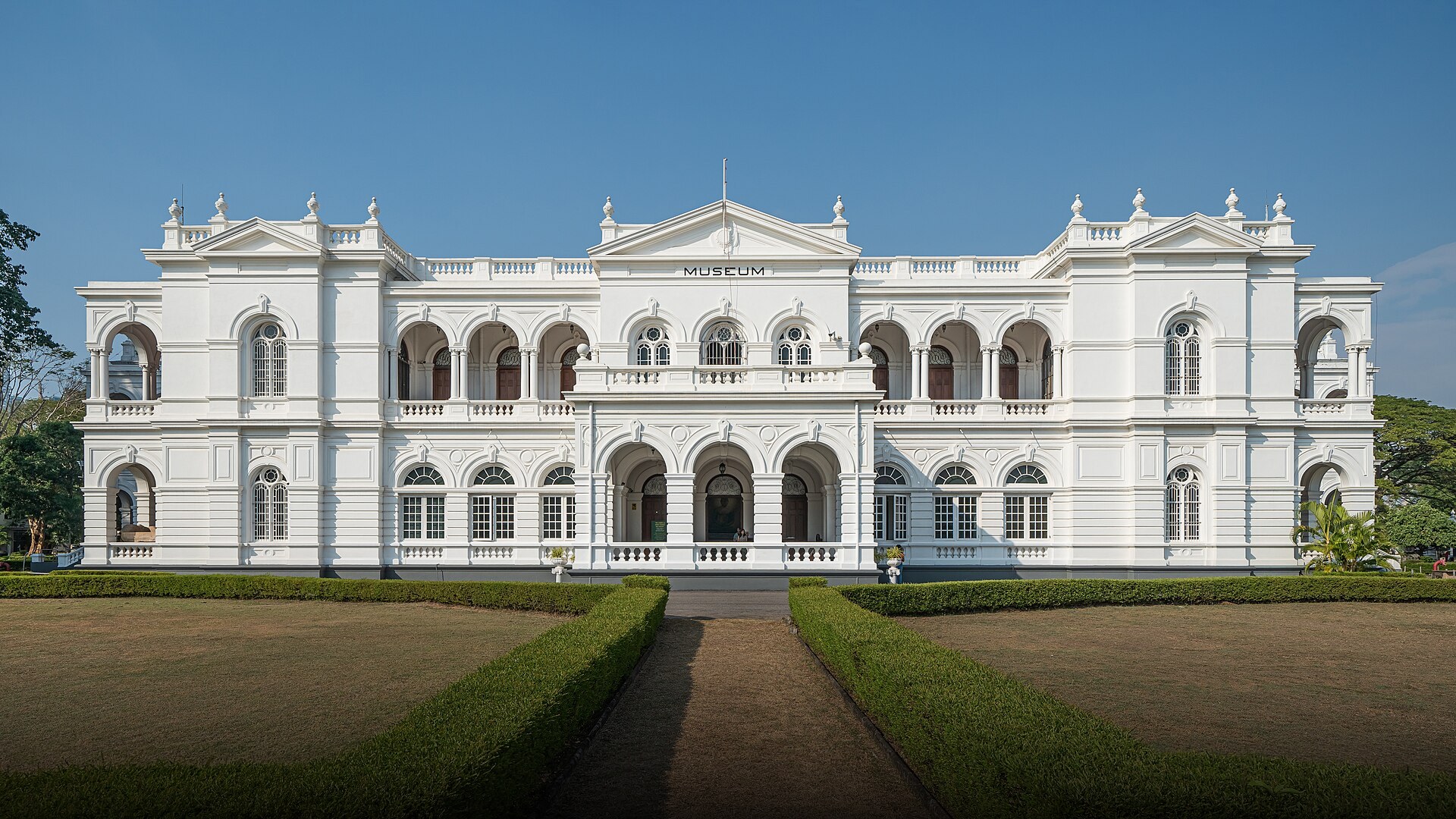 The historic white neoclassical facade of the National Museum of Colombo in Sri Lanka surrounded by manicured lawns.