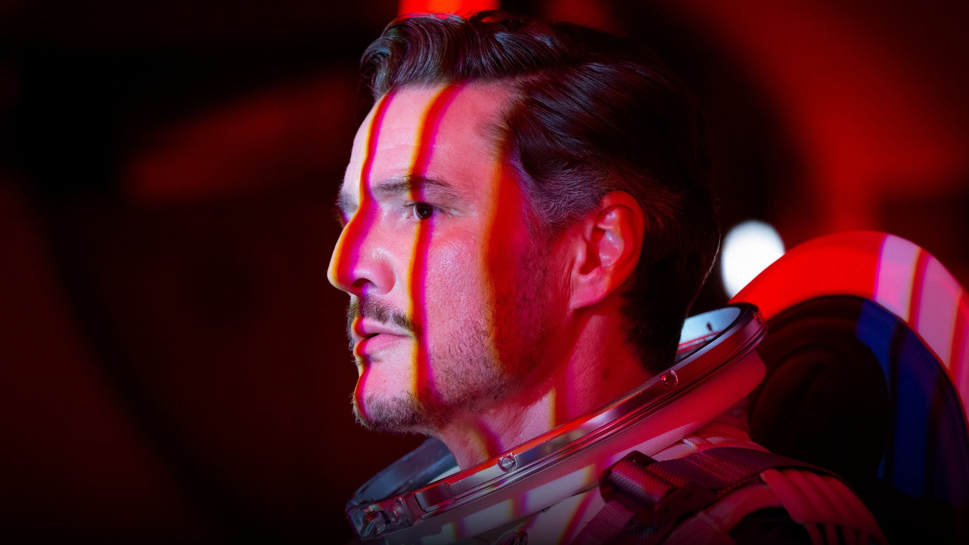 Pedro Pascal as Reed Richards in astronaut suit illuminated by dramatic red cockpit glow.