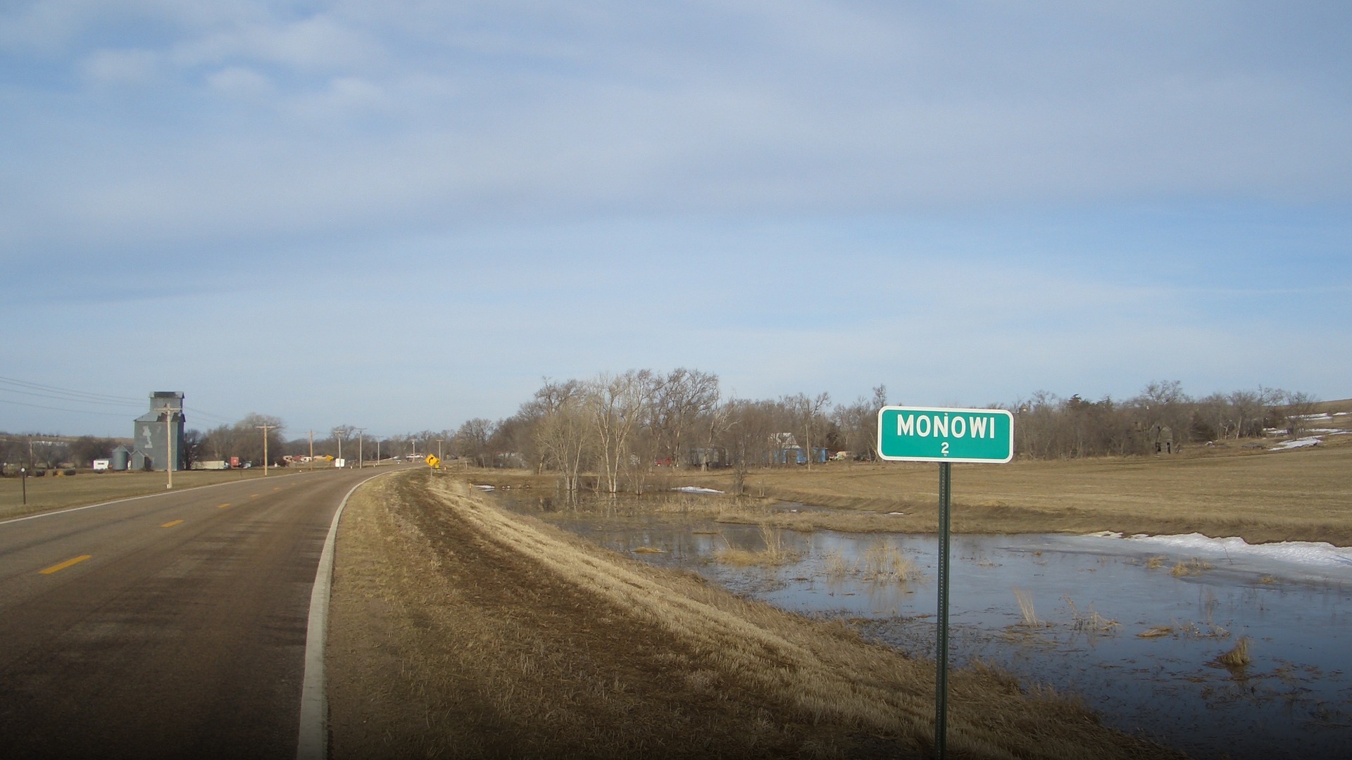 Green highway sign reading Monowi Population 1 along a rural Nebraska highway.