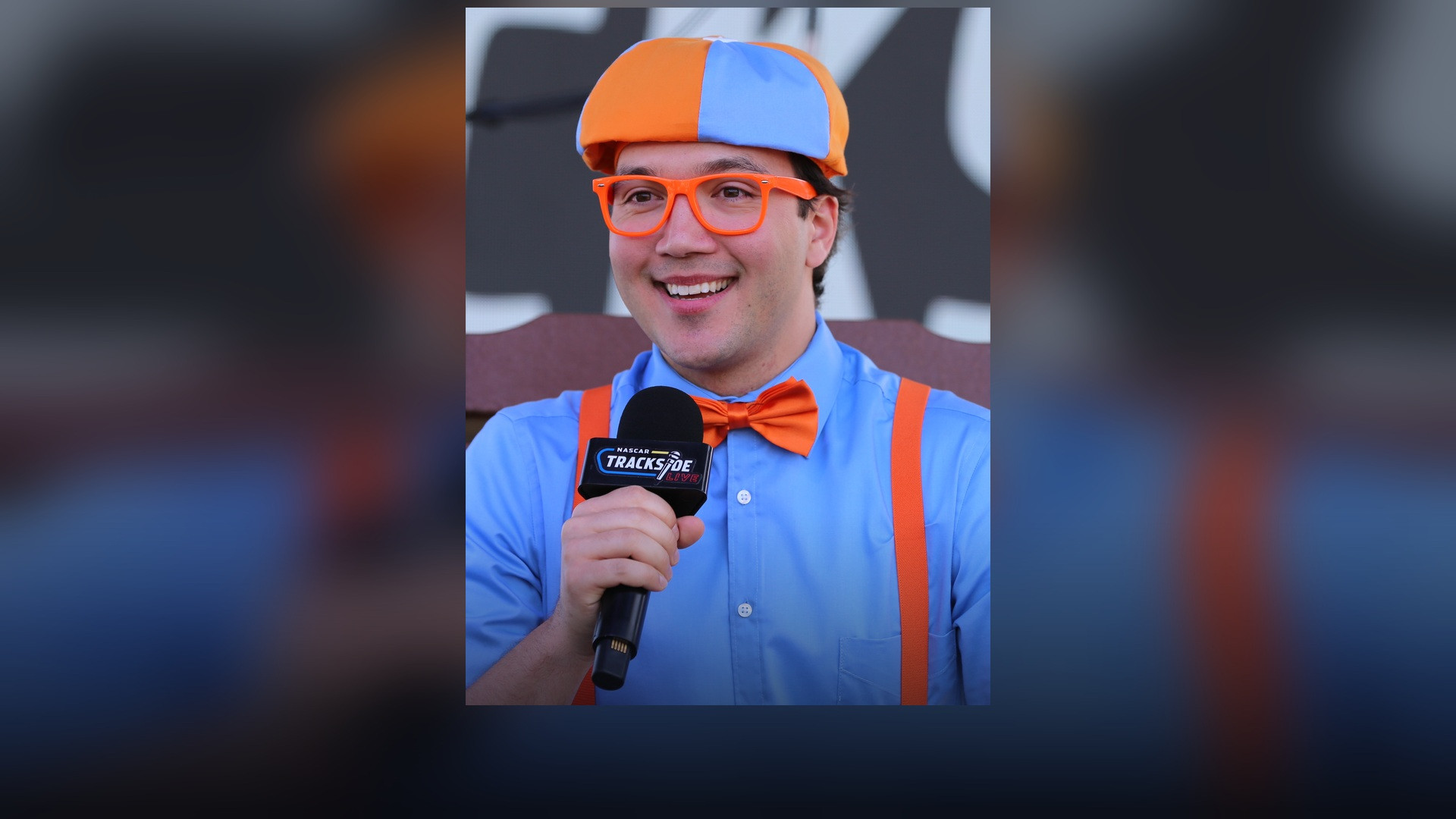 Stevin John performing in character as Blippi wearing orange glasses and blue cap.