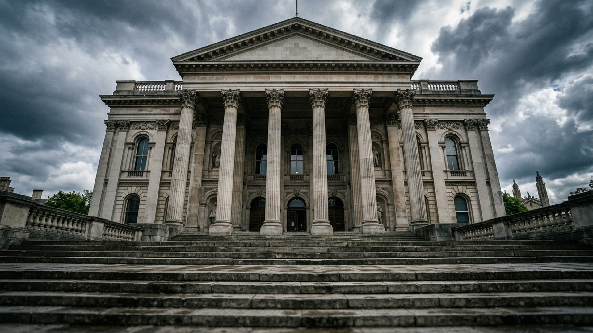 Grand stone facade and classical columns of a British magistrates court building under dramatic cloudy skies.