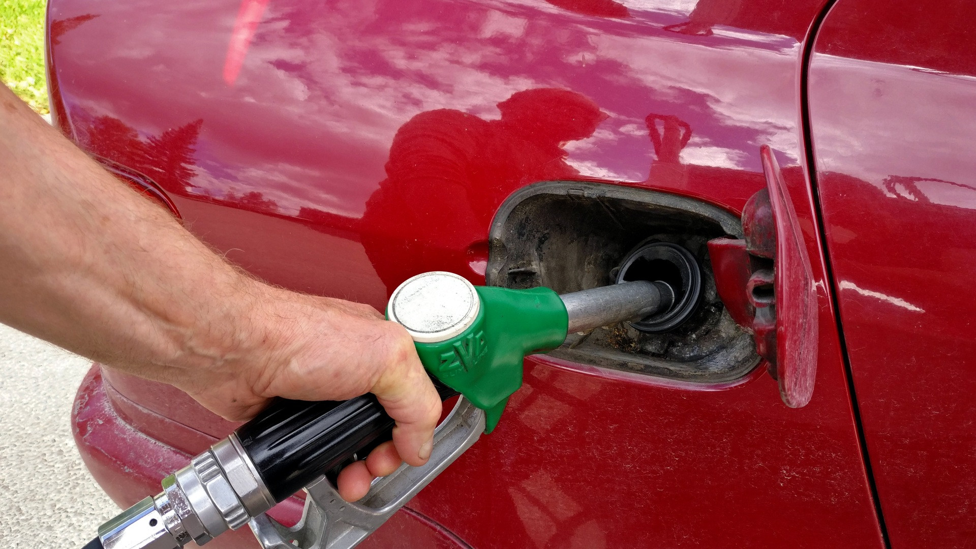 Macro photograph of a vehicle's metal fuel cap open with a nozzle dispenser inserting fuel.