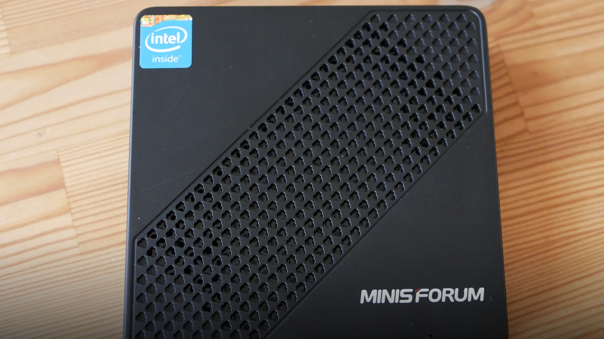 Compact black metal mini PC desktop computer shown from above displaying top vents and rear connectivity ports.