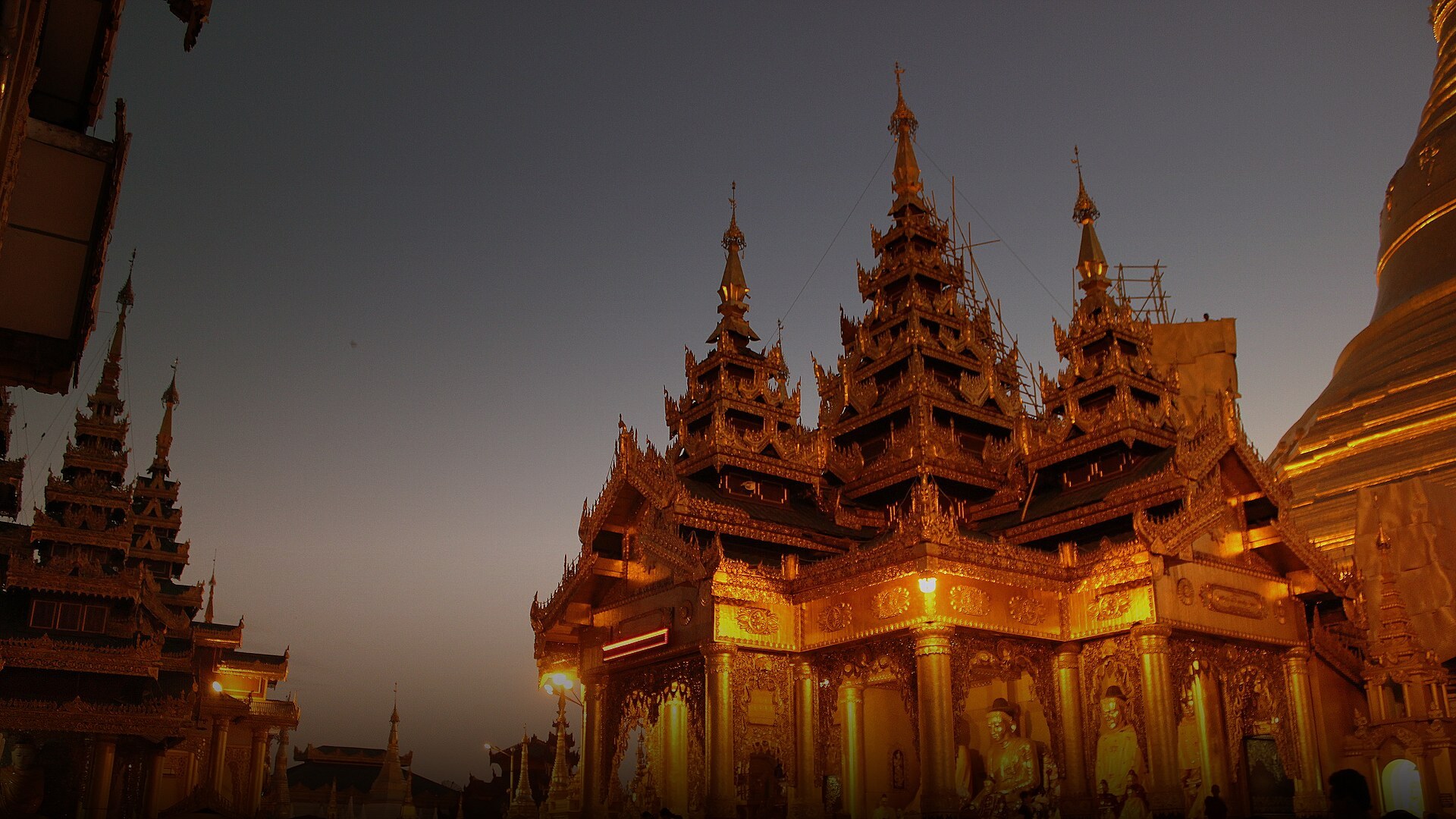 The monumental golden Shwedagon Pagoda glowing brilliantly at sunset against a dusk sky in Yangon, Myanmar.